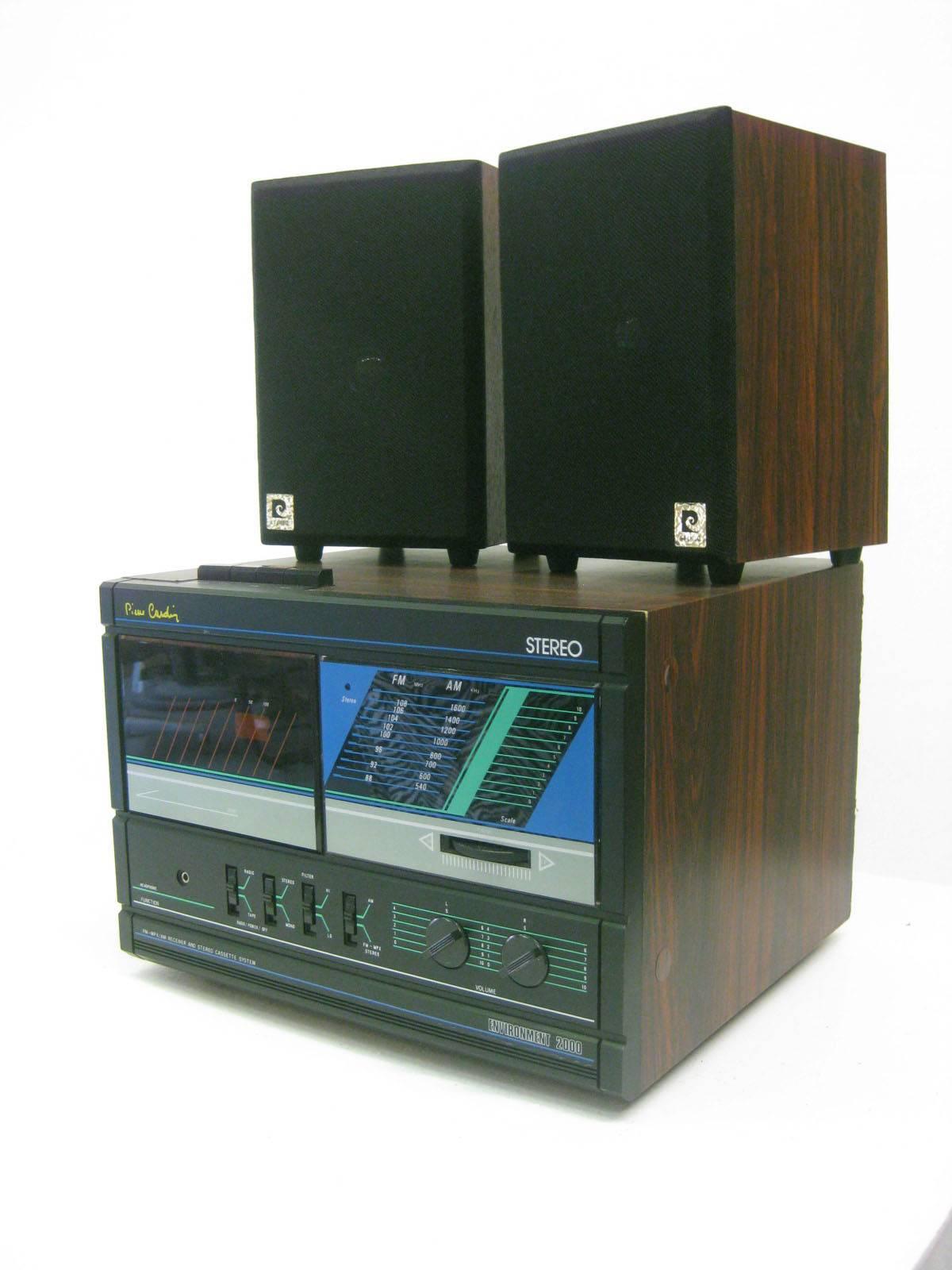 Stereo with two detached speakers by Pierre Cardin. AM/FM and Cassette. Dark wood case and very 1980s design. Speakers are 5.5 W x 6 D x 8.5 H individually.