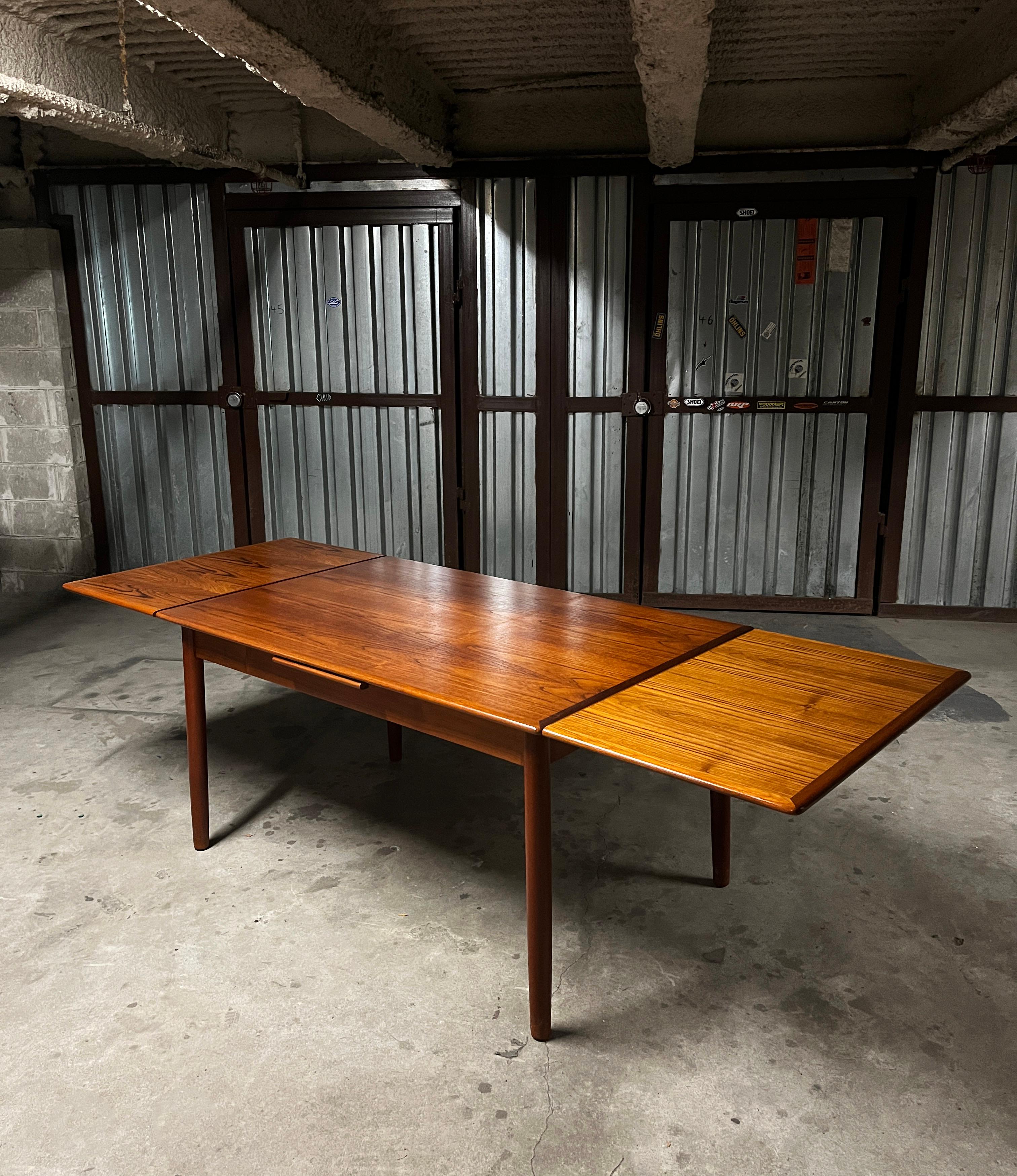 Incredibly Beautiful and practical Danish modern Am Mobler Teak Extending Dining Table (1960s). This table is very well constructed and very sturdy. The two side leaves slide under the main table top and sit flush when not being used. When closed it