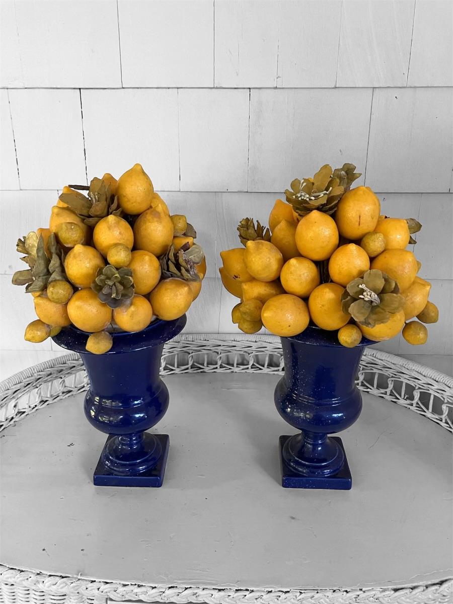 Limones de la Costa Amalfitana en jarrones azules de piedra artificial. Paquetes vintage de limones de imitación de aspecto muy real y vibrante mezclados con alcachofas de imitación de piña. Magnífica presentación de la dolce vita de la isla de