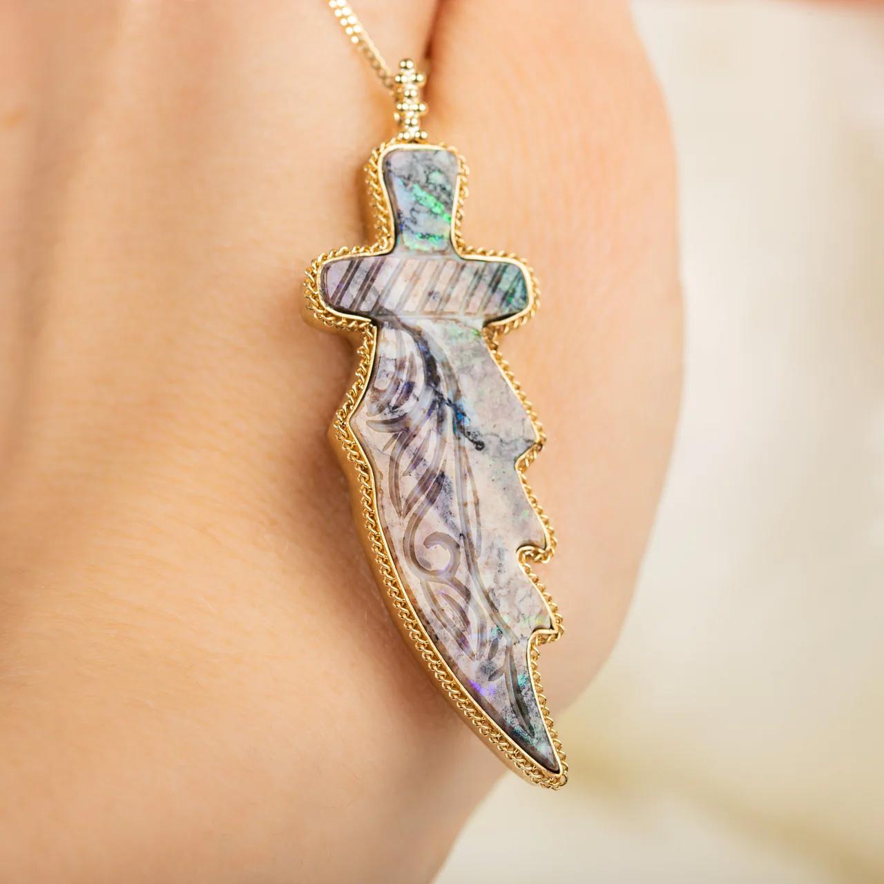 This Andamooka Opal has been expertly carved into the shape of an abstract dagger. The stone’s vibrant colorway of dark reddish purple over cream with clouds of orange and brown punctuated with flashes of electric green makes this Andamooka Opal