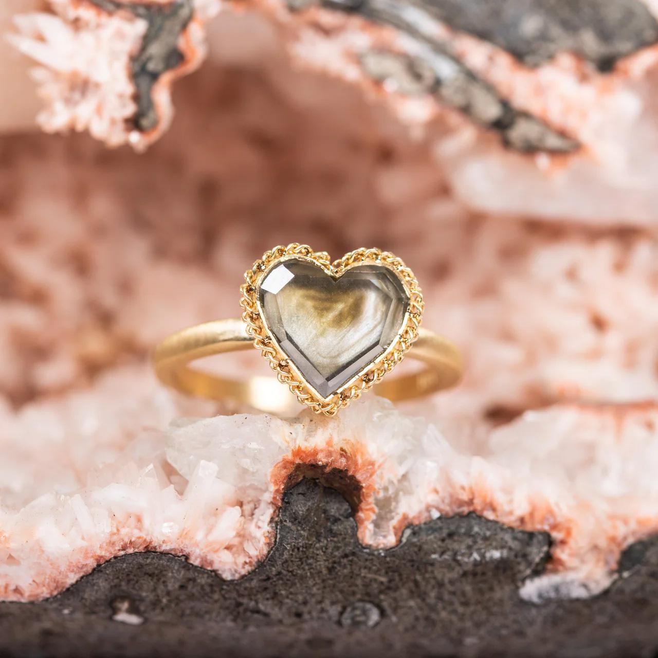 This extraordinary ring features a custom-cut Diamond in the shape of a heart. Its generous, subtle facets flicker with reflected light, a subtle dancing glimmer that comes alive with your every hand movement. This remarkable Diamond is set in a