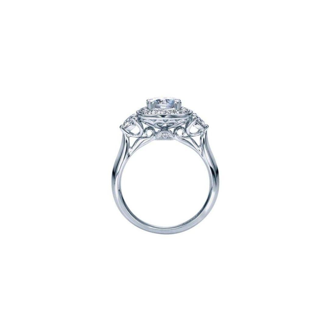 Classic design with a vintage touch makes this ring an interesting twist on a traditional three stone combination. The center stone is elaborated by a beautiful diamond halo with a cushion shape. Two round diamonds add brilliance from the sides of