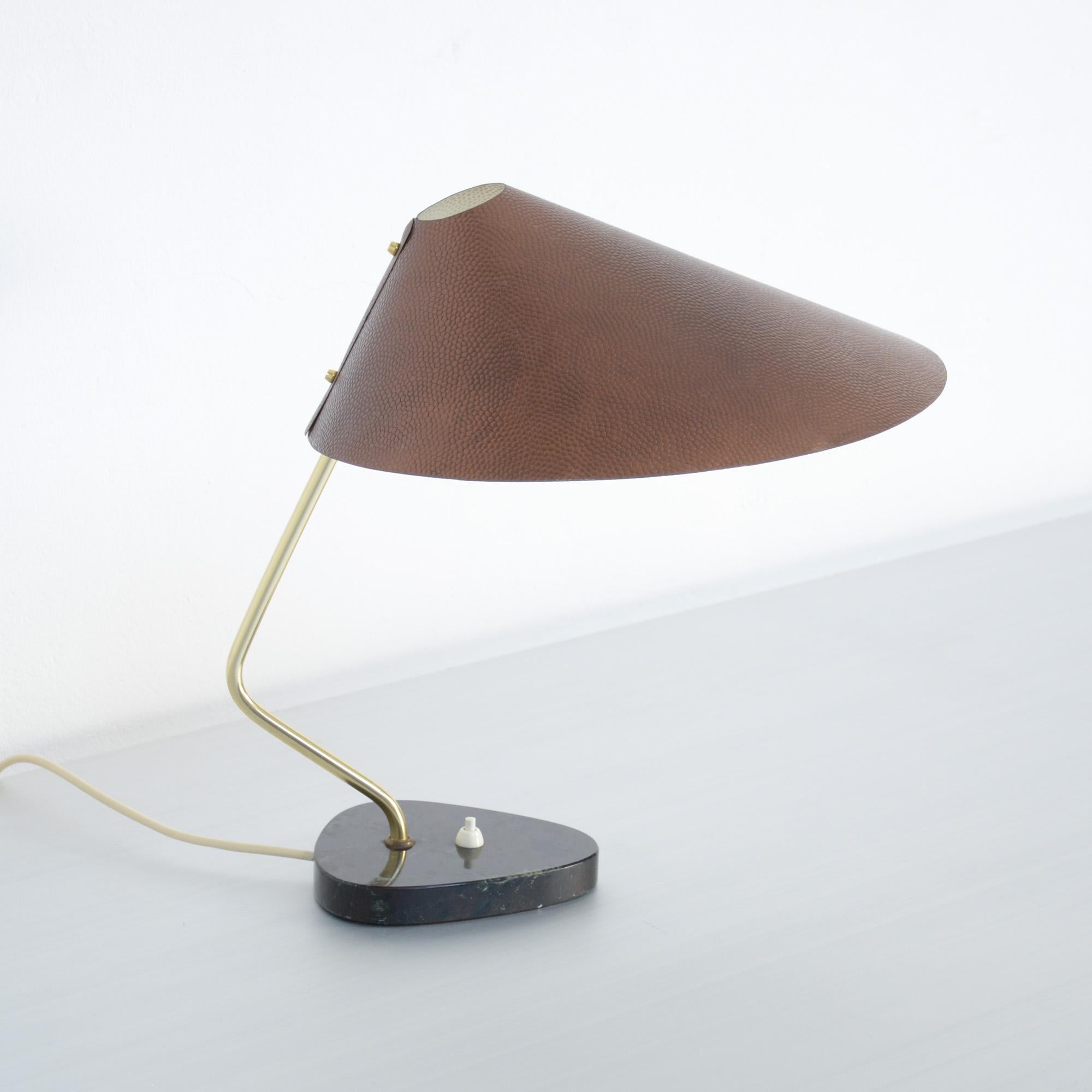 This amazing 1950s desk lamp is made in Germany.
It is a sophisticated design, with a asymmetrical black marble base, a brass modulated stem and an amazing copper-colored hammered aluminum shade.
This lamp is complete authentic from the 1950s and