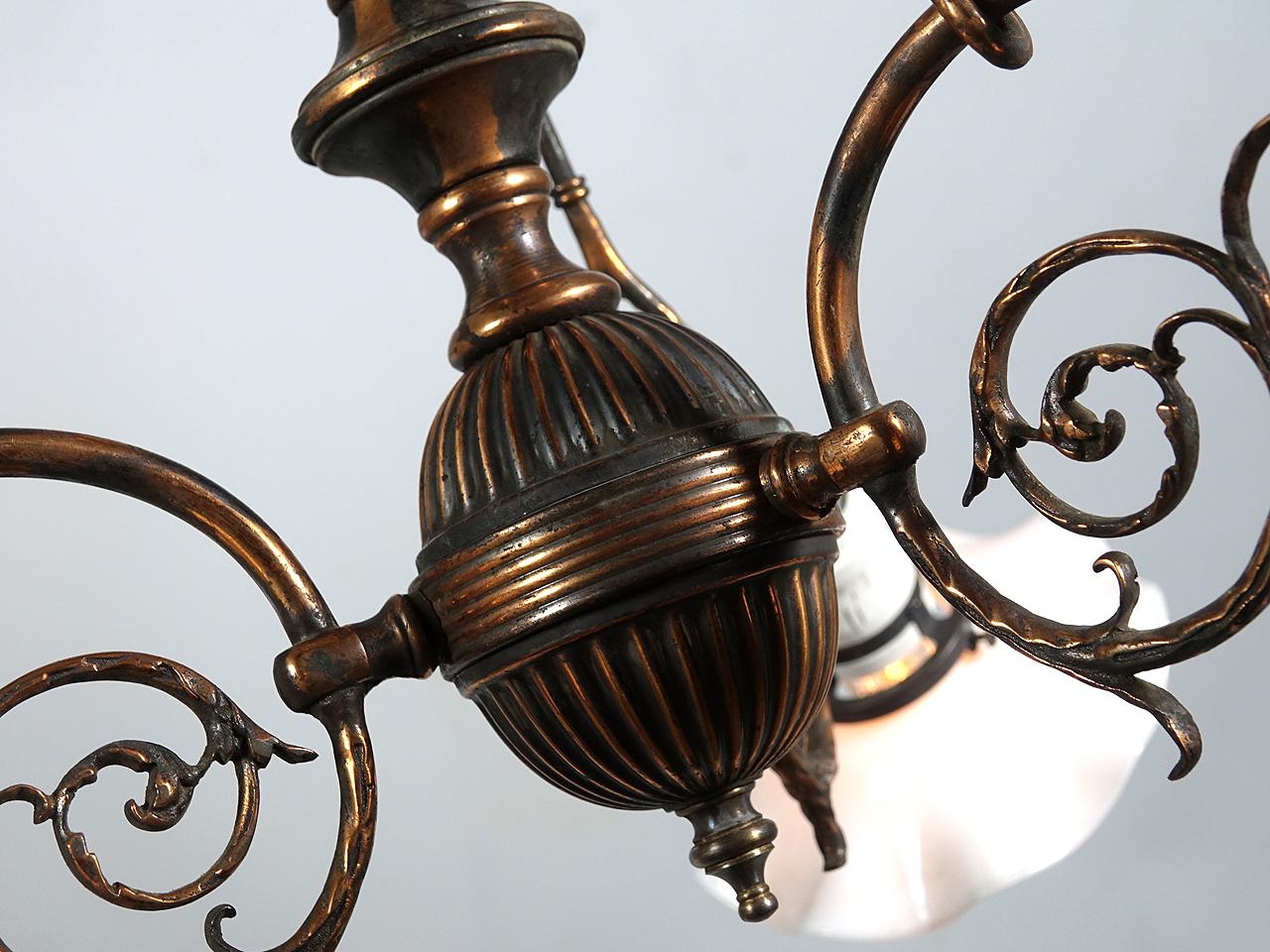 This is a late 1800s gas lamp that has been wired for electric. This fixture has everything going for it and is a real gem. The japanned finish, white porcelain sockets with tiny milk glass ruffled shades, decorative cast arms and support rods make