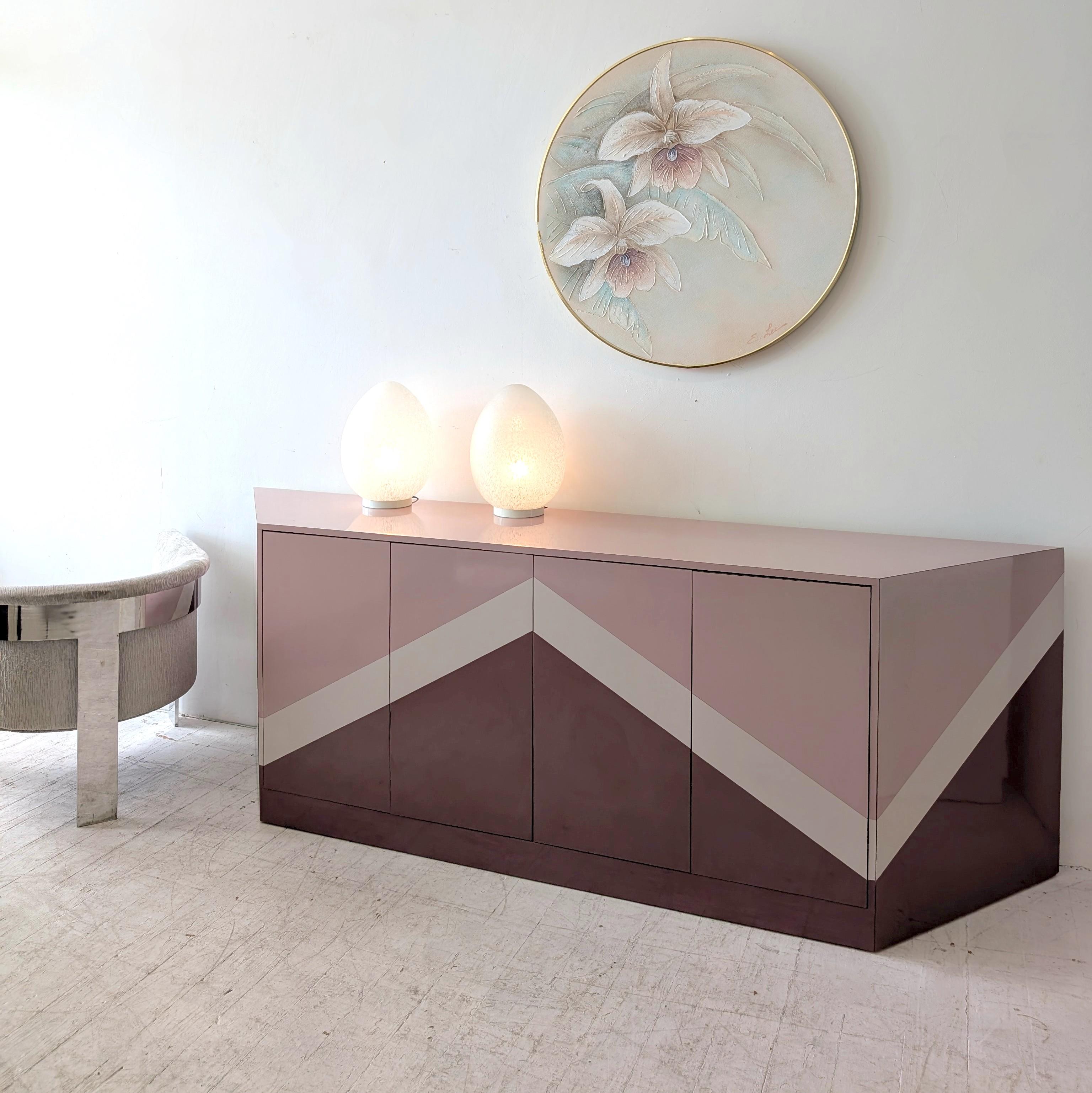 Etonnant buffet postmoderne zig zag en forme de trapèze anguleux, USA 1980.
Revêtu de 3 couleurs de stratifié brillant - rose pâle, rose mauve plus foncé, marron. 
Quatre portes à bouton-poussoir s'ouvrent sur des étagères intérieures et un tiroir.