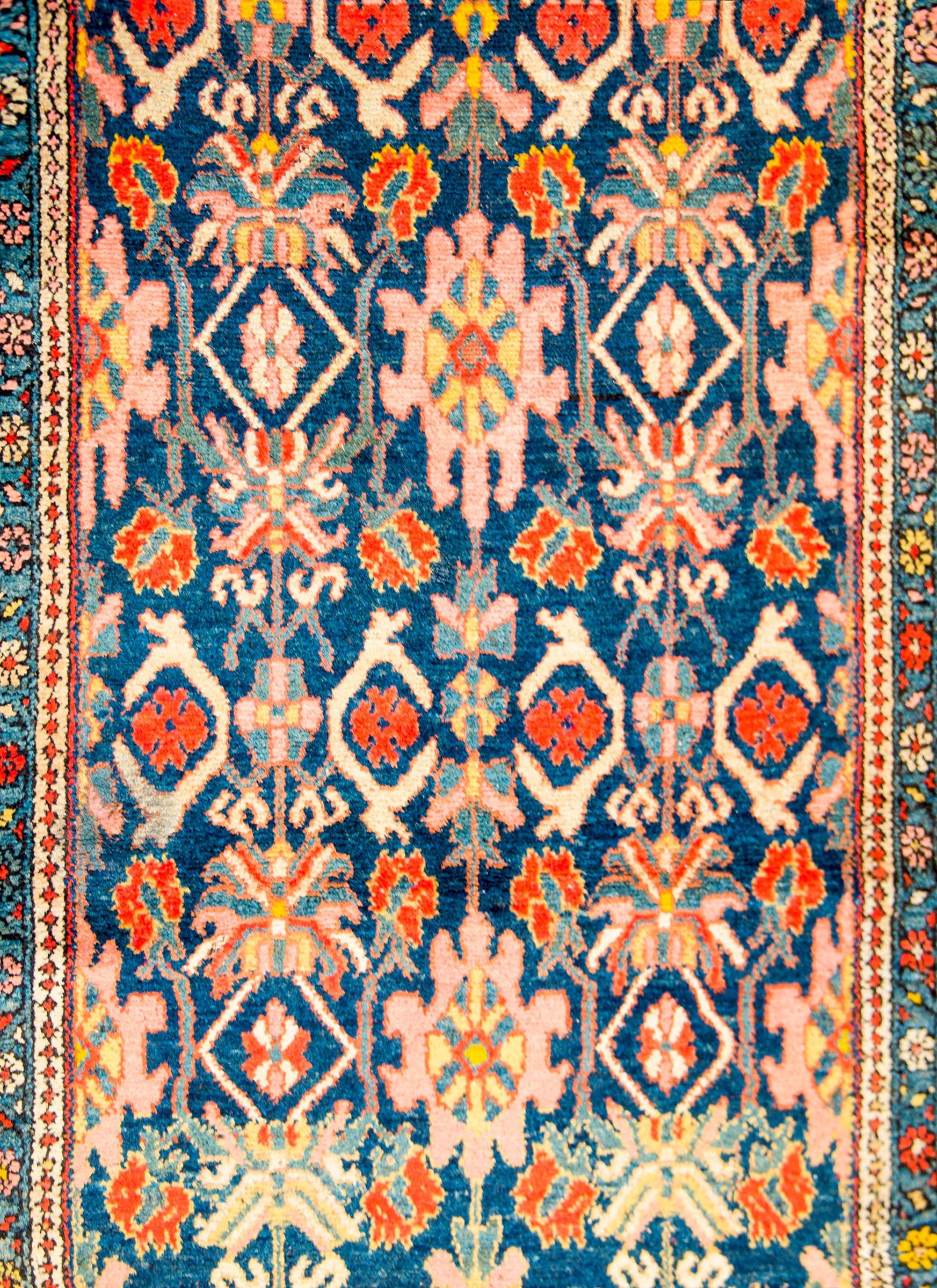 An amazing early 20th century Persian Malayer rug with an all-over trellised floral, leaf, and vine pattern woven in pink, yellow, crimson, and light indigo, on a dark indigo background. The border is composed with one central floral and vine stripe