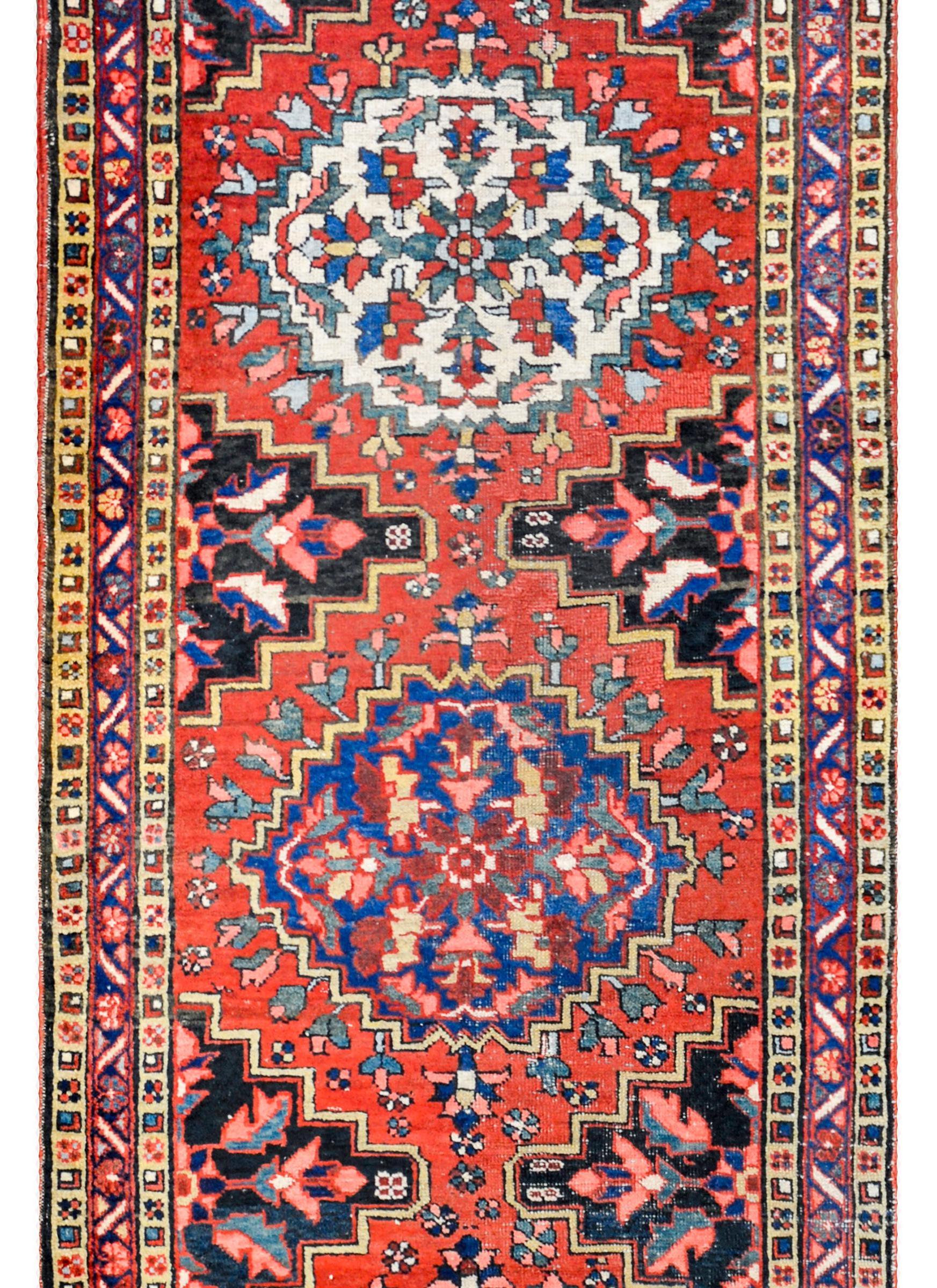 An amazing early 20th century Persian Bakhtiari runner with five large multicolored medallions on a crimson background. The border is complex, with a central stylized floral patterned stripe flanked by matching petite stylized floral stripes.