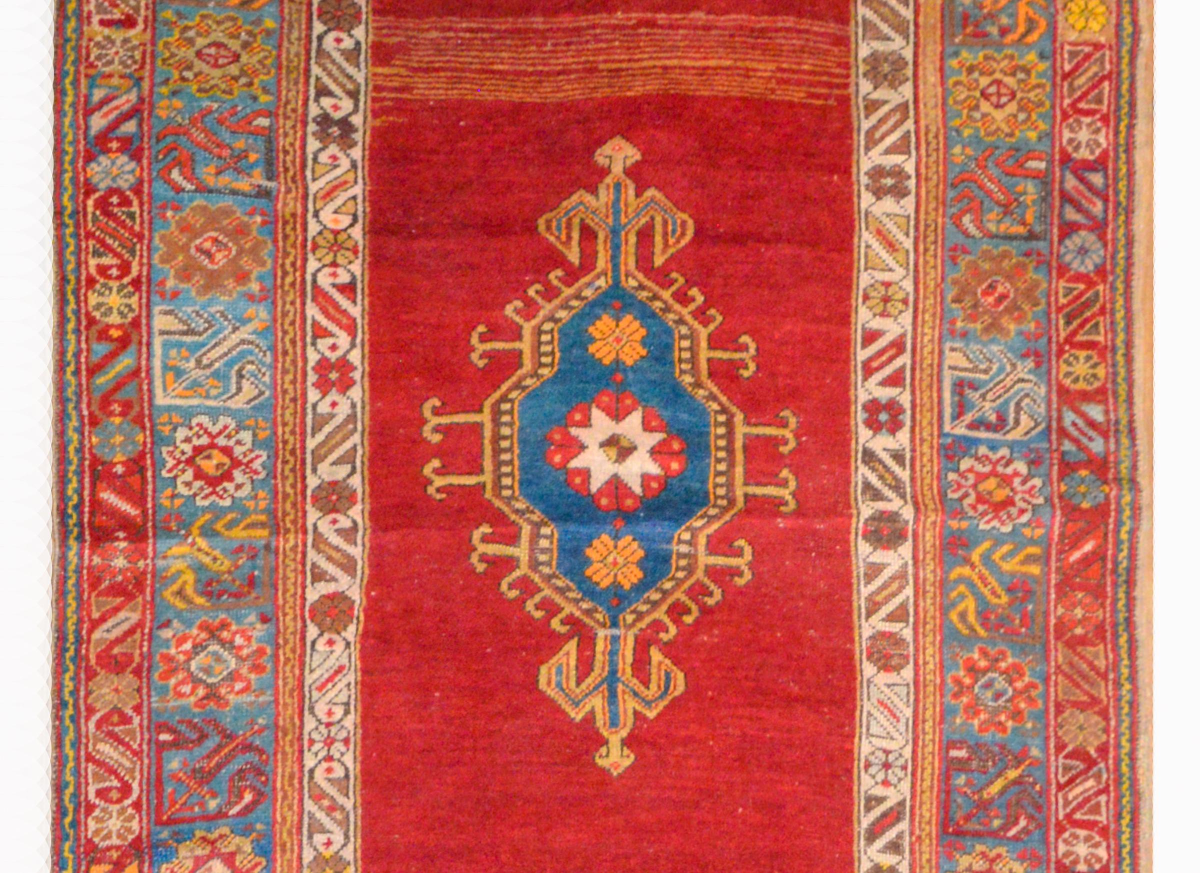 An amazing early 20th century Turkish Konya runner with three large indigo diamond medallions abasing a bold crimson background, and surrounded by a wide border containing multiple floral and stylized floral patterned stripes, all woven in crimson,