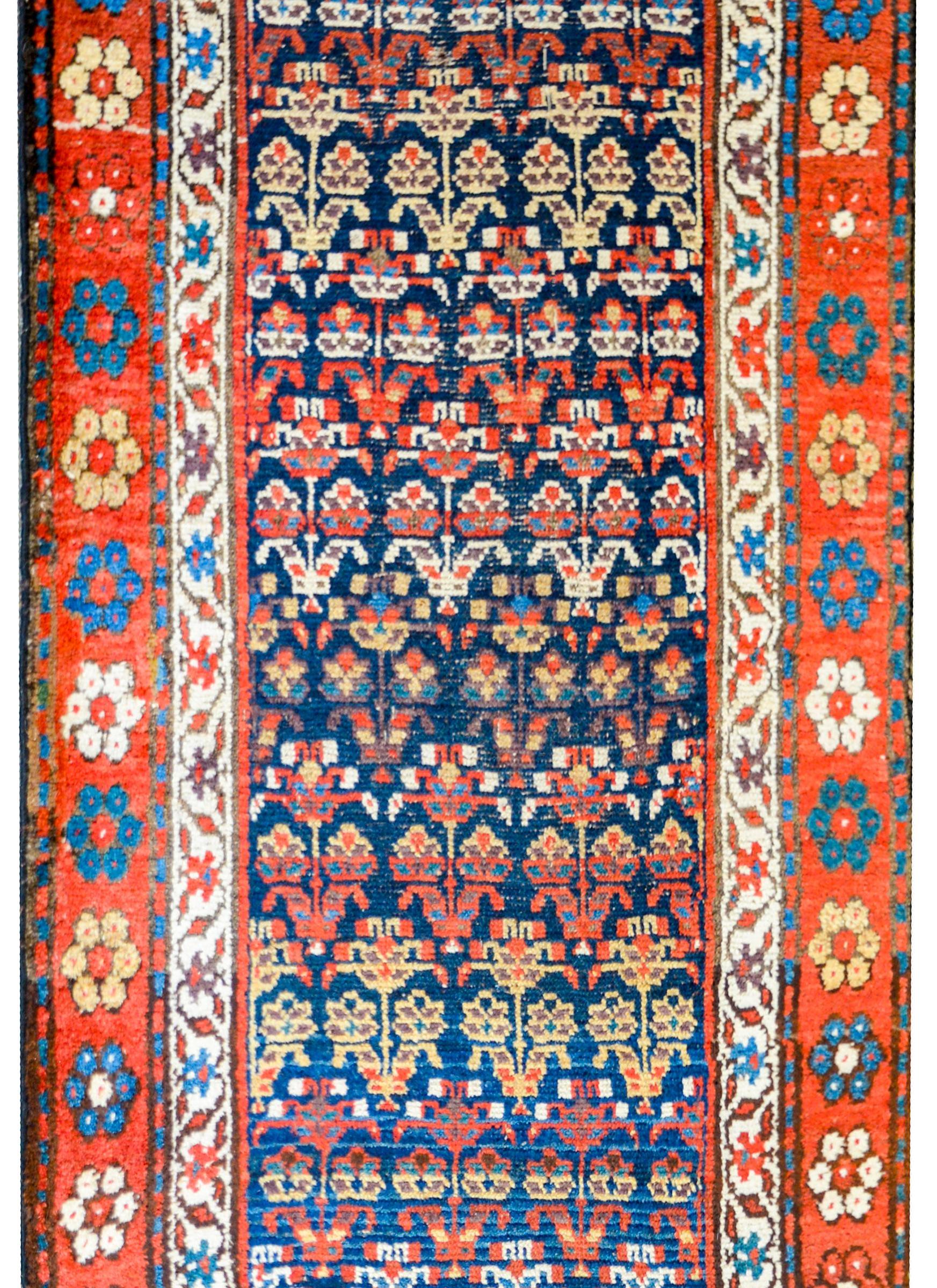 An amazing early 20th century Northwest Persian runner with an all-over multicolored tree-of-life pattern woven in light and dark indigo, gold, crimson, and white, on a dark indigo background. The border is composed with repeated bold flowers on a