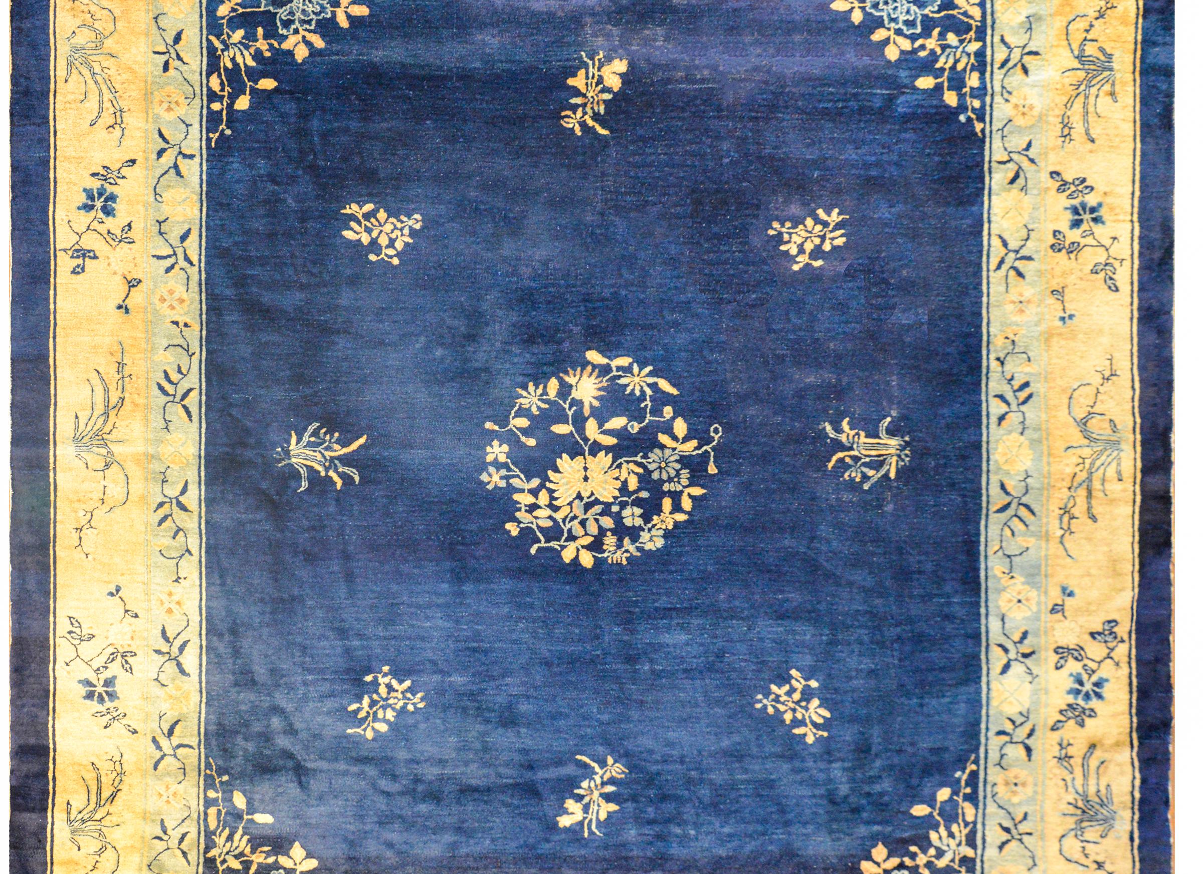 An amazing early 20th century Chinese Peking rug with a central floral medallion amidst a field of additional flowers on a beautiful indigo field, surrounded by a wide cream colored and pale indigo colored borders with pairs of goldfish in each