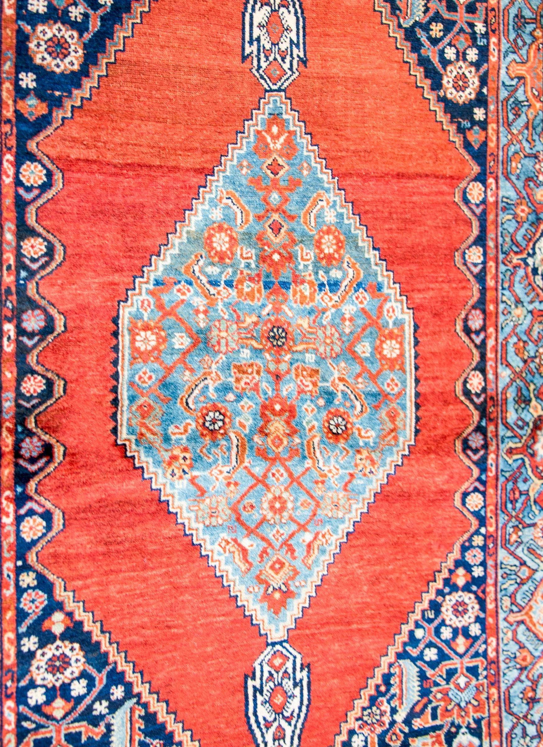 Tappeto persiano Seneh dei primi del Novecento con un meraviglioso medaglione a diamante intrecciato con un motivo floreale a traliccio, vite e foglie multicolore, su uno sfondo indaco chiaro, che vive su uno sfondo cremisi. Il bordo è ampio, con