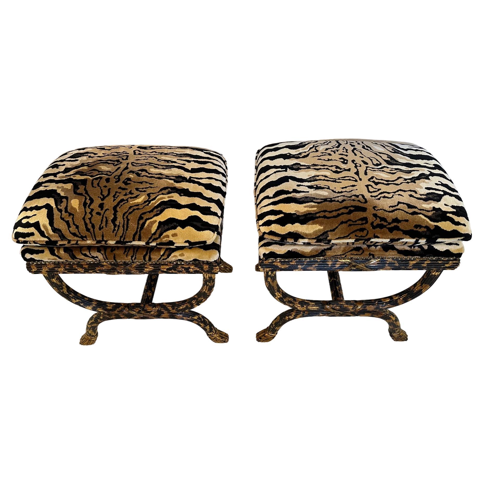 Stunning pair of custom, neoclassical style ottomans by William Switzer, renowned  furniture make since 1952.  Glam animal print velvet with hand painted gilding and black fluted wood base, antique nailheads and hoof feet. A rare find
