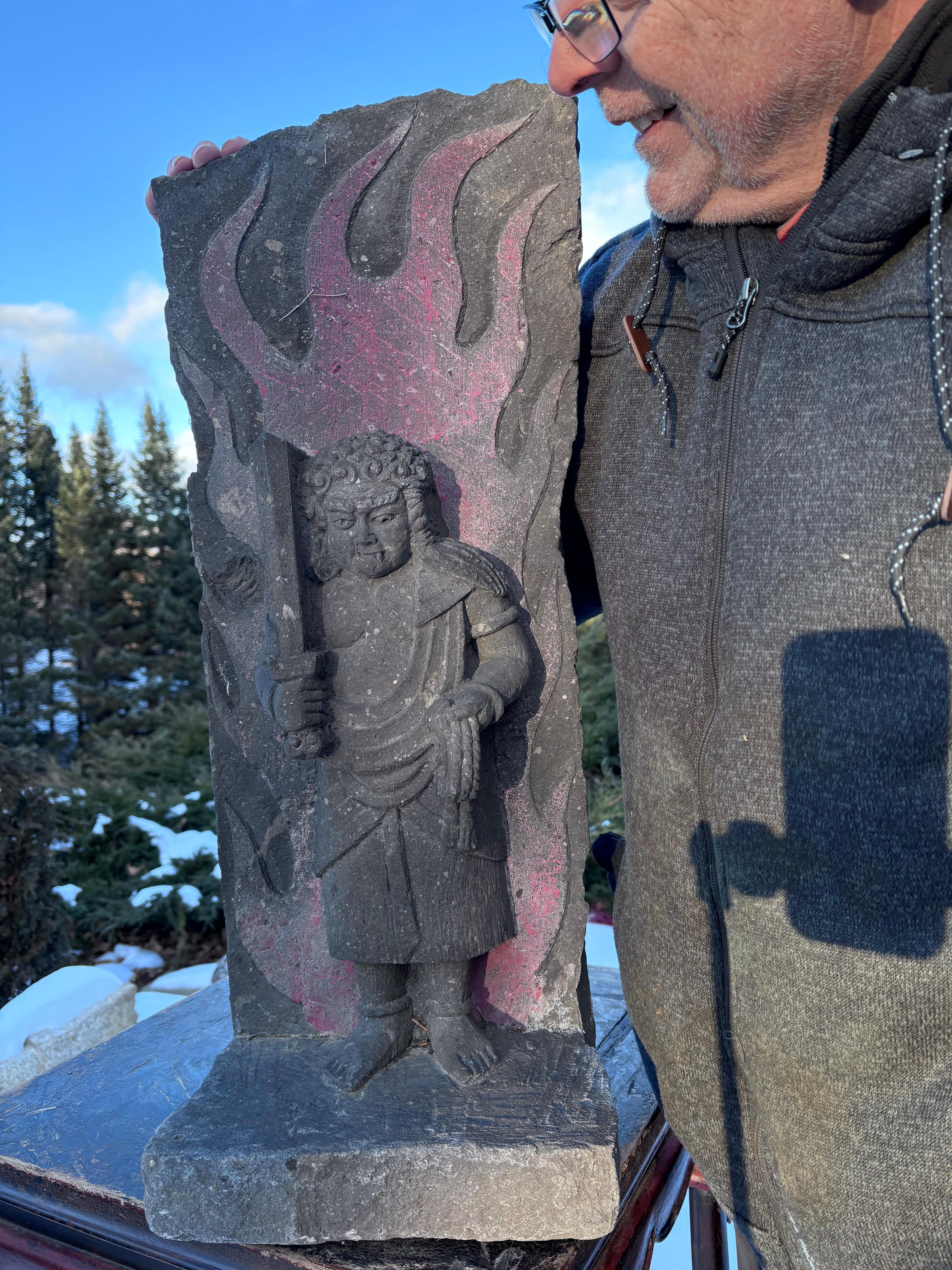 A very old circa 19th century Japanese stone guardian protector in a monumental , hand painted unusual  form Fudo-Myo (Skt. Alacanatha) seated upon a rock-form dais and backed by a red painted flame mandorla, the right hand holding a sword and the
