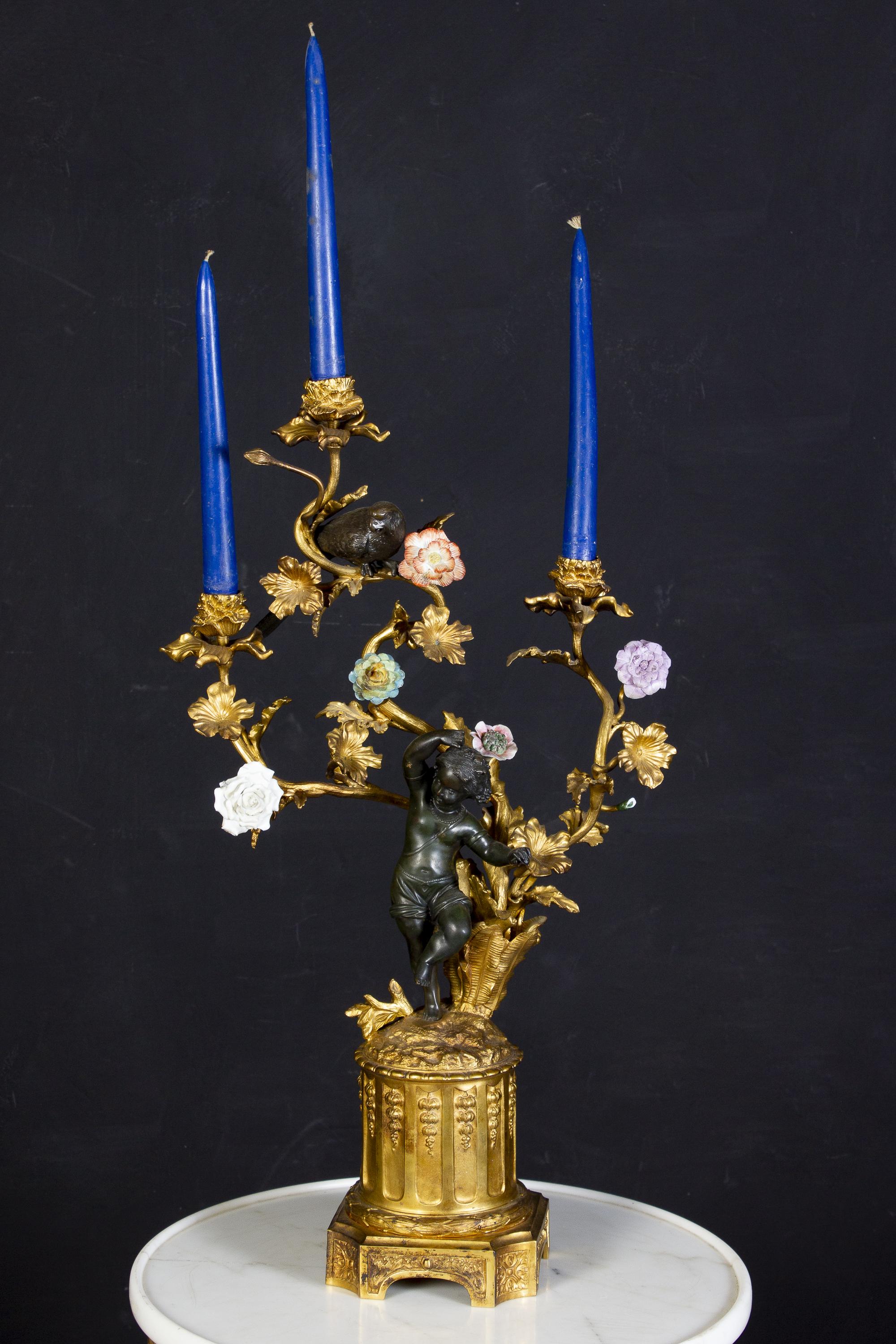 Une paire de candélabres français du 19e siècle en bronze et bronze doré, chacun avec un délicieux bronze foncé dansant des personnages putto et des perroquets tenant en l'air trois branches de bougies à volutes avec des fleurs colorées en