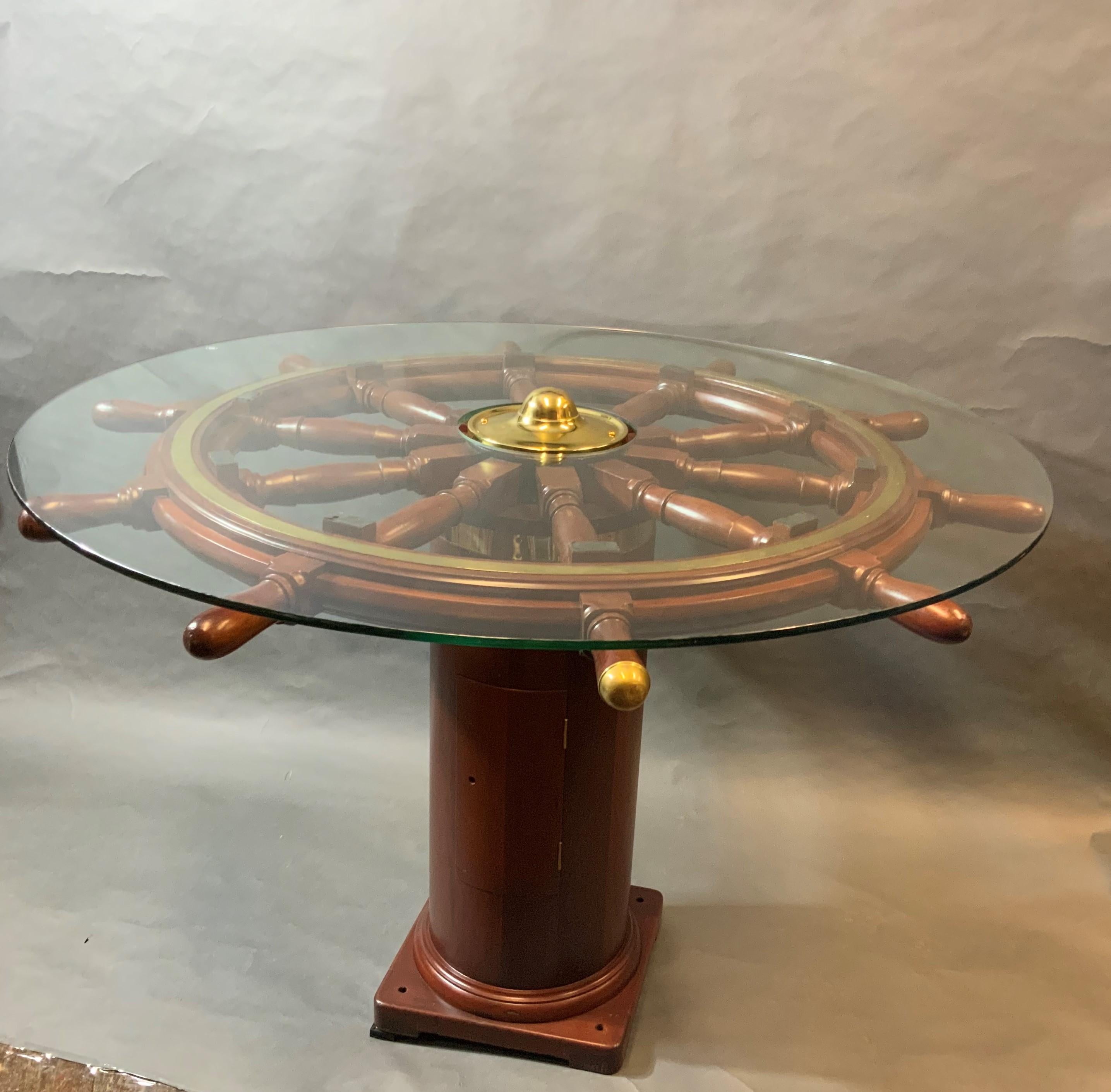 Varnished mahogany early twentieth century ships wheel that has been sanded, stained and refinished. With inlaid brass trim ring and hub. Mounted onto a ship's binnacle base that has also been wonderfully restored as well. With tempered glass