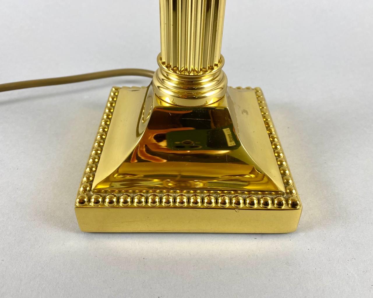 La luxueuse lampe de table est fabriquée dans un style classique, le pied de la lampe est en laiton ciselé et doré, tout comme l'abat-jour avec quatre appliques.

 La base en forme de piédestal se transformant en colonne. Le sommet de la lampe est