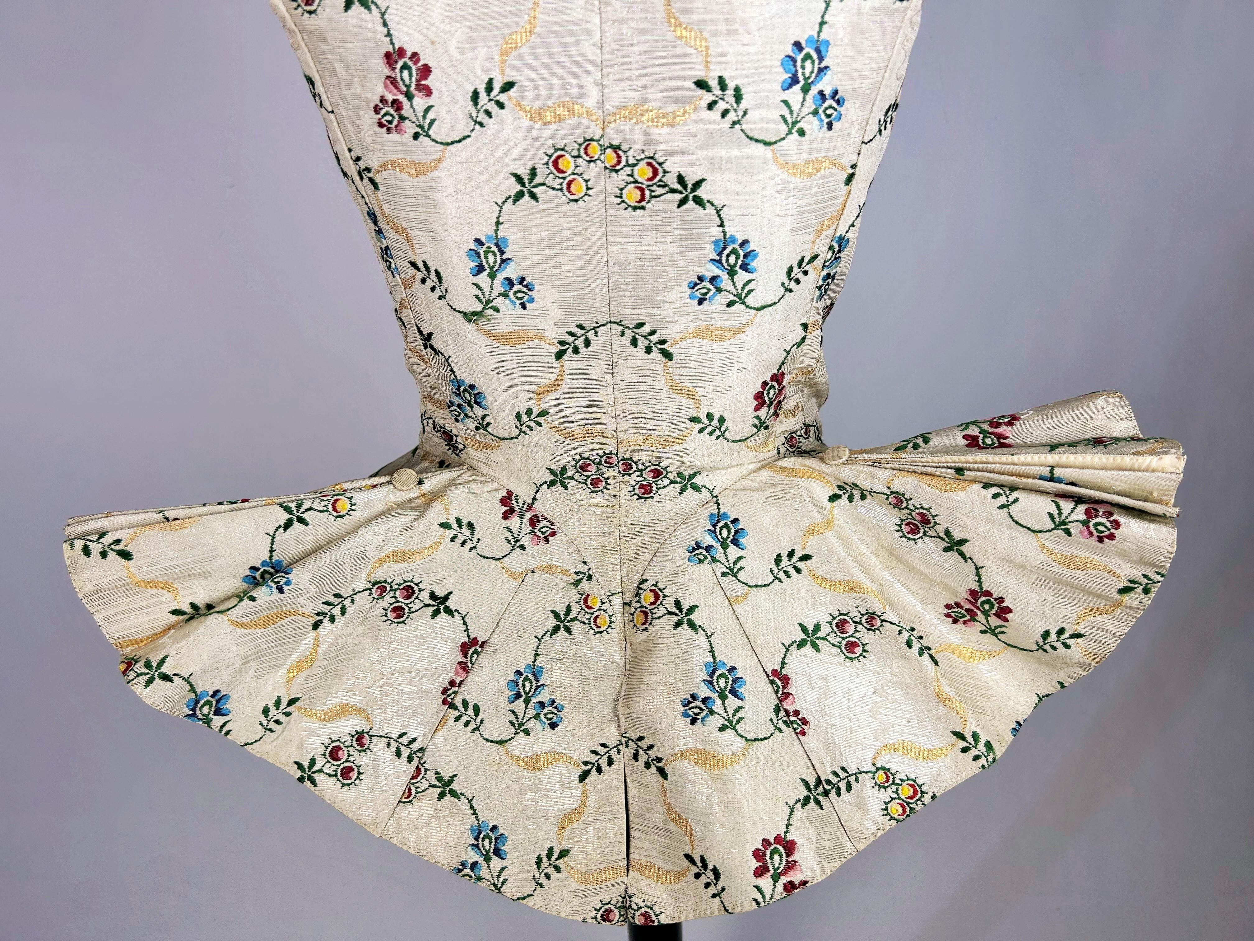 Circa 1750
England or Europe

Sleeveless bodice and long pleated basques in silver cloth, lampas in silver thread. Rich polychrome silk brocade with wood berry design and undulating scrolls of gold thread. Skilfully tailored with long pleated