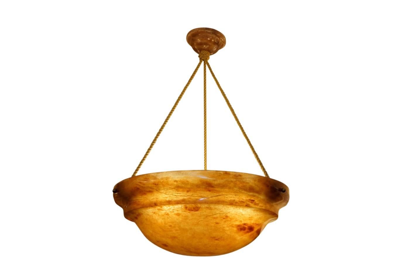 A natural, amber toned alabaster is a warm sleek pendant with crystal, rather than mineral, veining. Suspended on three electrified ropes from a matching alabaster canopy, the light fixture holds three LED bulbs of any wattage or three 75 watt