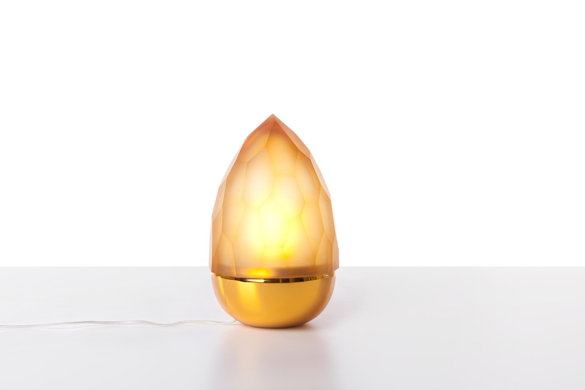 Amber and gold Mr. Flame table lamp by Dechem Studio.
Dimensions: D 18 x H 28 cm.
Materials: glass.
Also available: different colours available.

Two completely contrasting and differently manufactured glass shapes create Mr. Flame Table Lamp.
