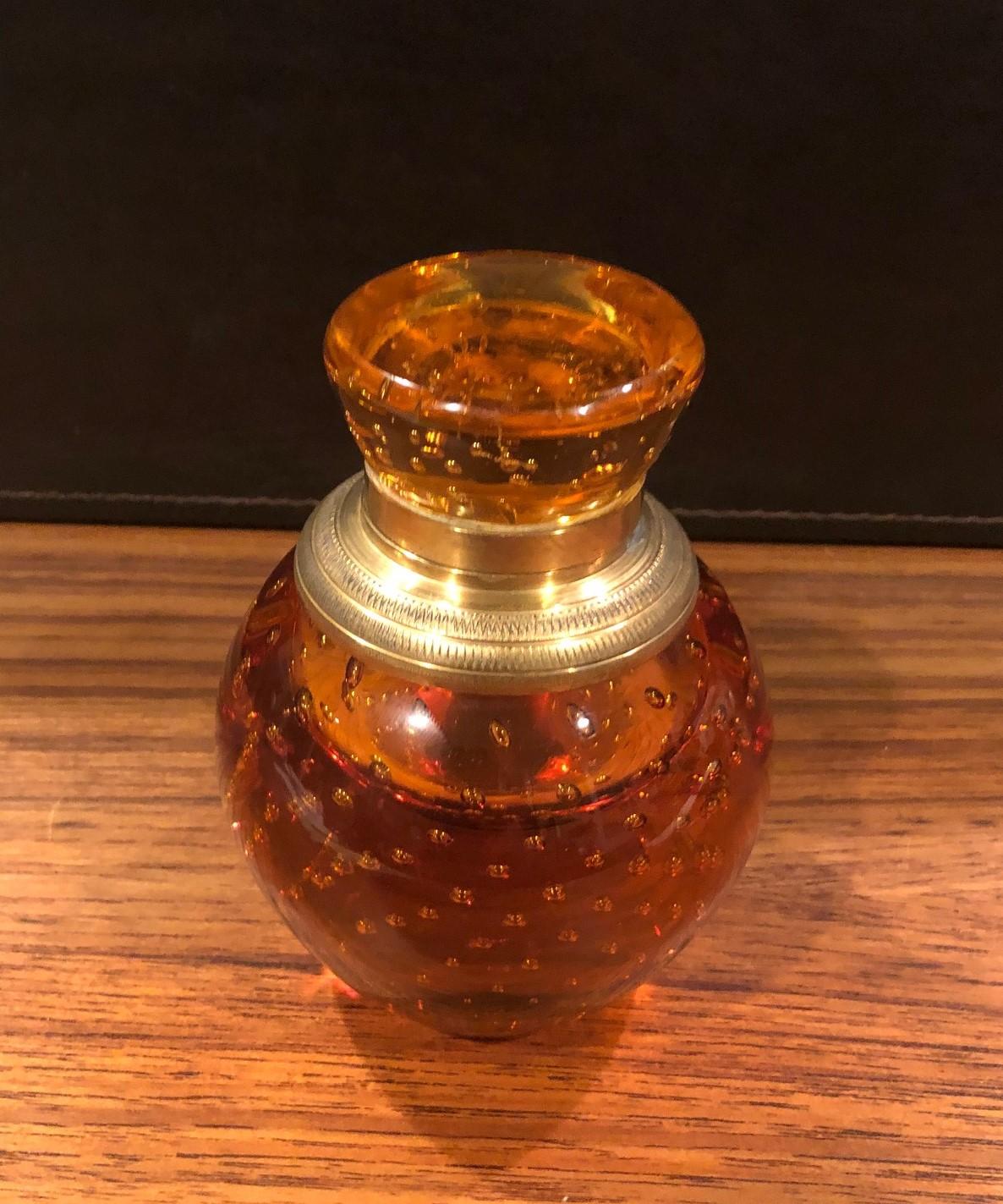 Rare amber bubble glass cylindrical inkwell with brass lid by John Armer & Co., circa 1940s. The well is very heavy and in very good condition with the exception of a very tiny flea bite chip on the underside of the well.


