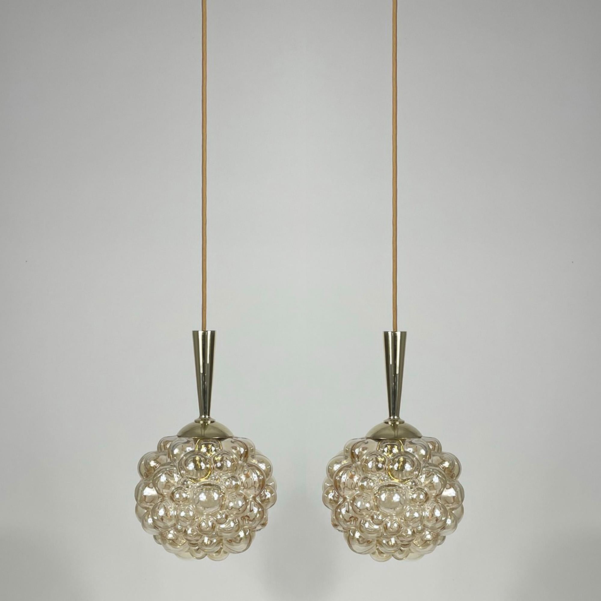 These midcentury Space Age pendant lights were designed during the 1960s by Helena Tynell and Heinrich Gantenbrink and manufactured by Glashuette Limburg in Germany. They feature amber bubble glass lampshades with a glossy finish and brass hardware.