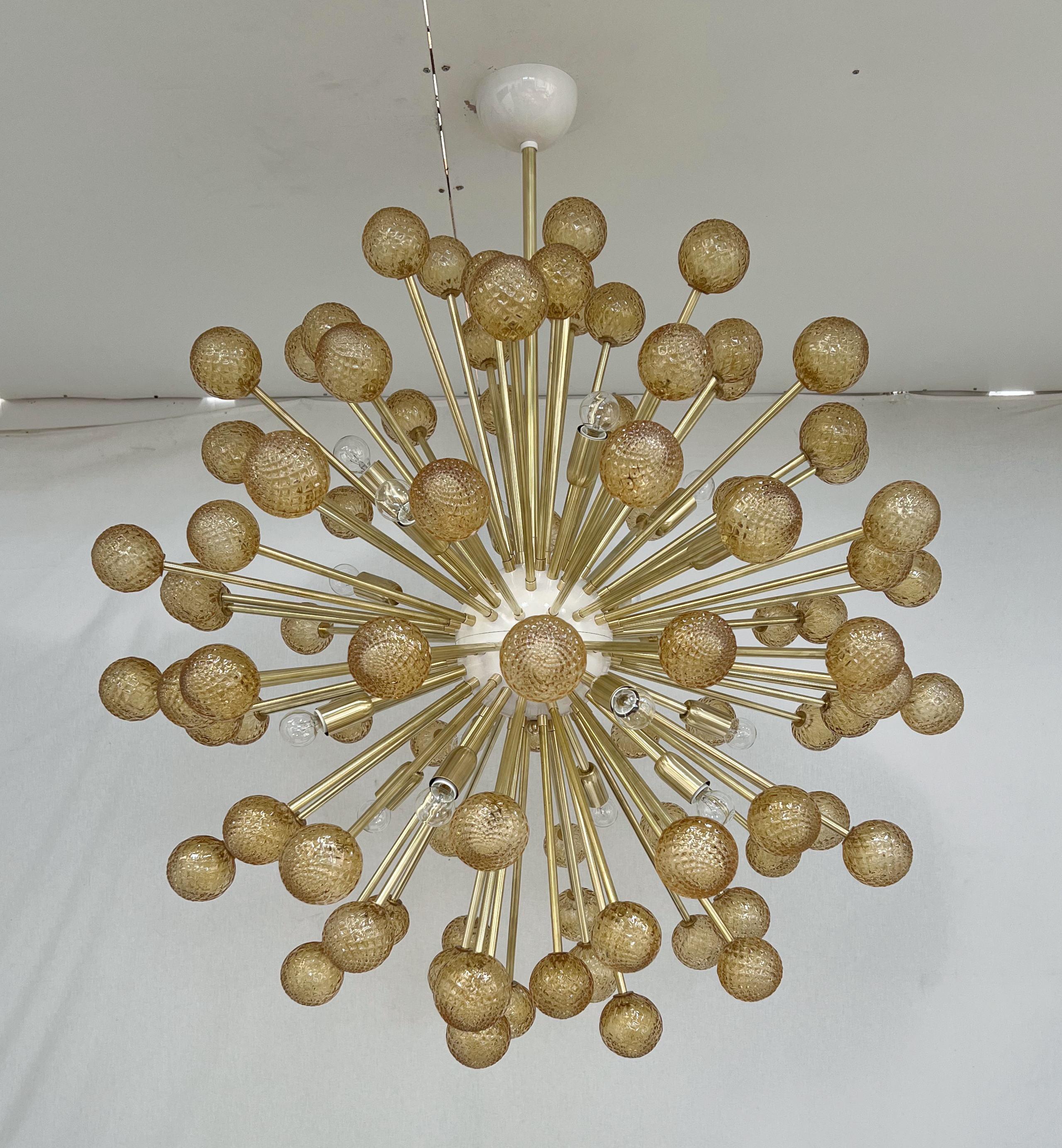 Italian modern sputnik chandelier with hand blown textured amber Murano glass spheres, mounted on unlacquered natural brass frame with cream enameled center / Designed by Fabio Bergomi for Fabio Ltd / Made in Italy
16 lights / E12 or E14 type / max