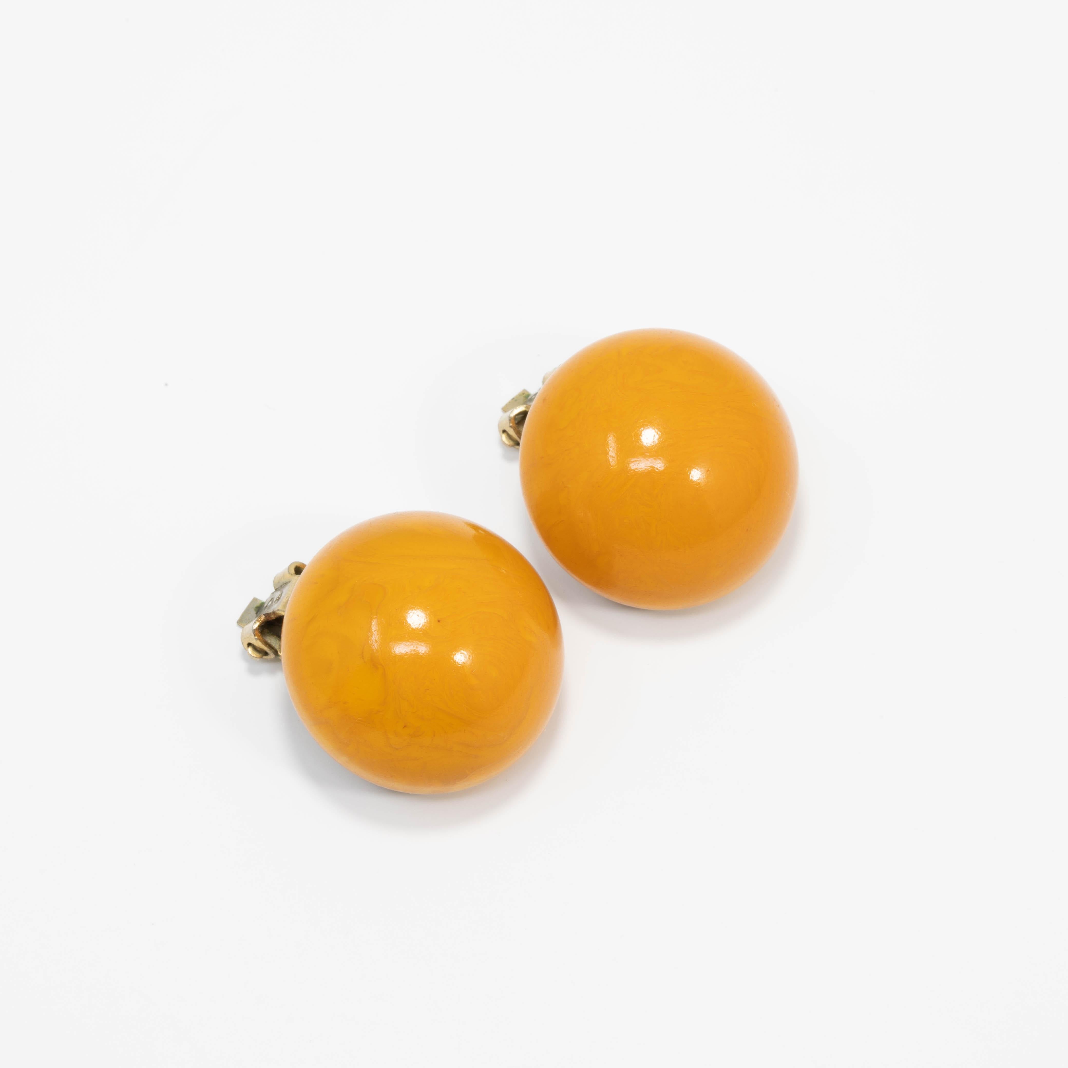 A pair of stylish vintage bakelite earrings. Each features an amber butterscotch yellow bakelite button set on brass-tone clip on hardware.

Circa early to mid 1900s.