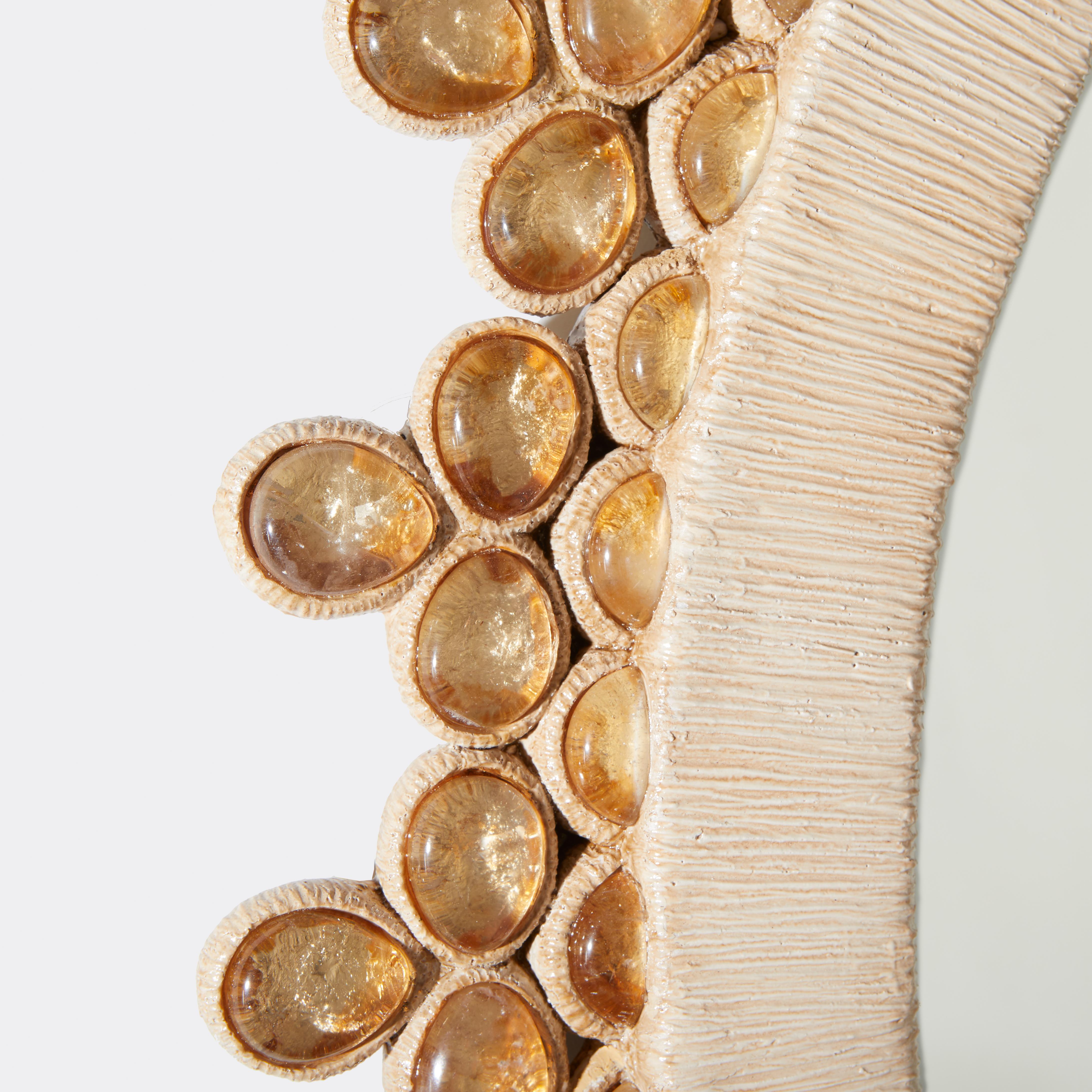 Lo specchio in cristallo di rocca Amber Cabochon, disegnato da David Duncan. Uno specchio rotondo con cornice in resina di Wood e pigmenti, fuso in sezioni e incastonato con ornamenti cabochon di cristallo di rocca a forma di ovale e di goccia. Ogni