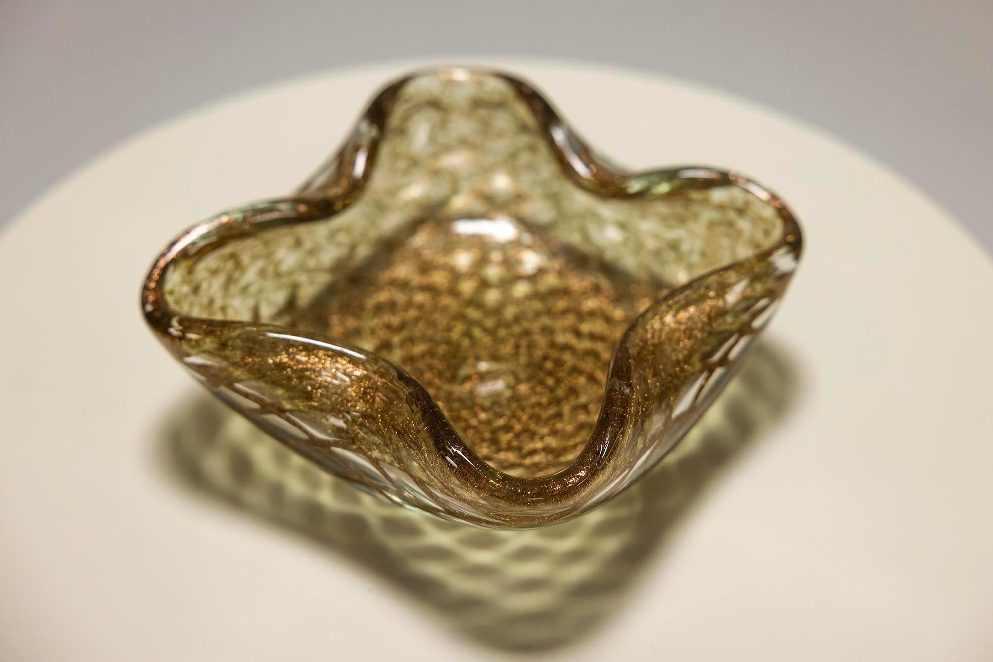 This Murano glass bowl, crafted in the 1960s, exemplifies the sophisticated artistry of mid-20th century Venetian glassmaking.

Design
Amber to brown in color, the bowl is richly infused with golden snippets, creating a shimmering effect that