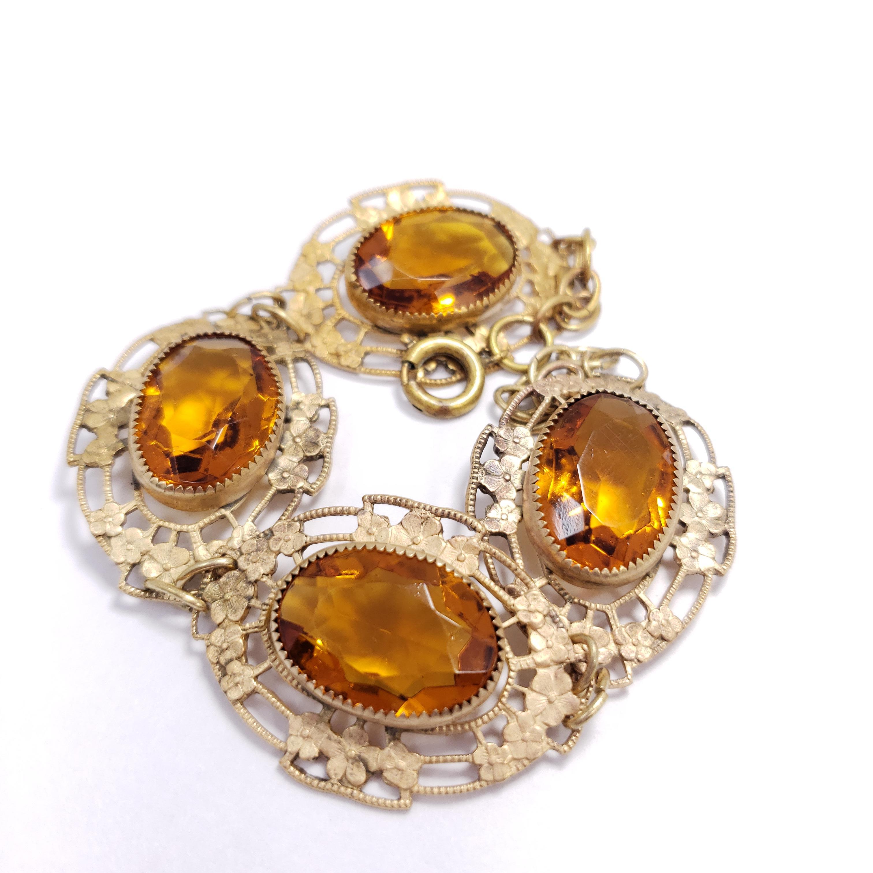An elegant vintage bracelet. Features four floral-themed, brass-tone links, each with a mesmerizing, open-back, amber crystal.

Spring ring closure.
