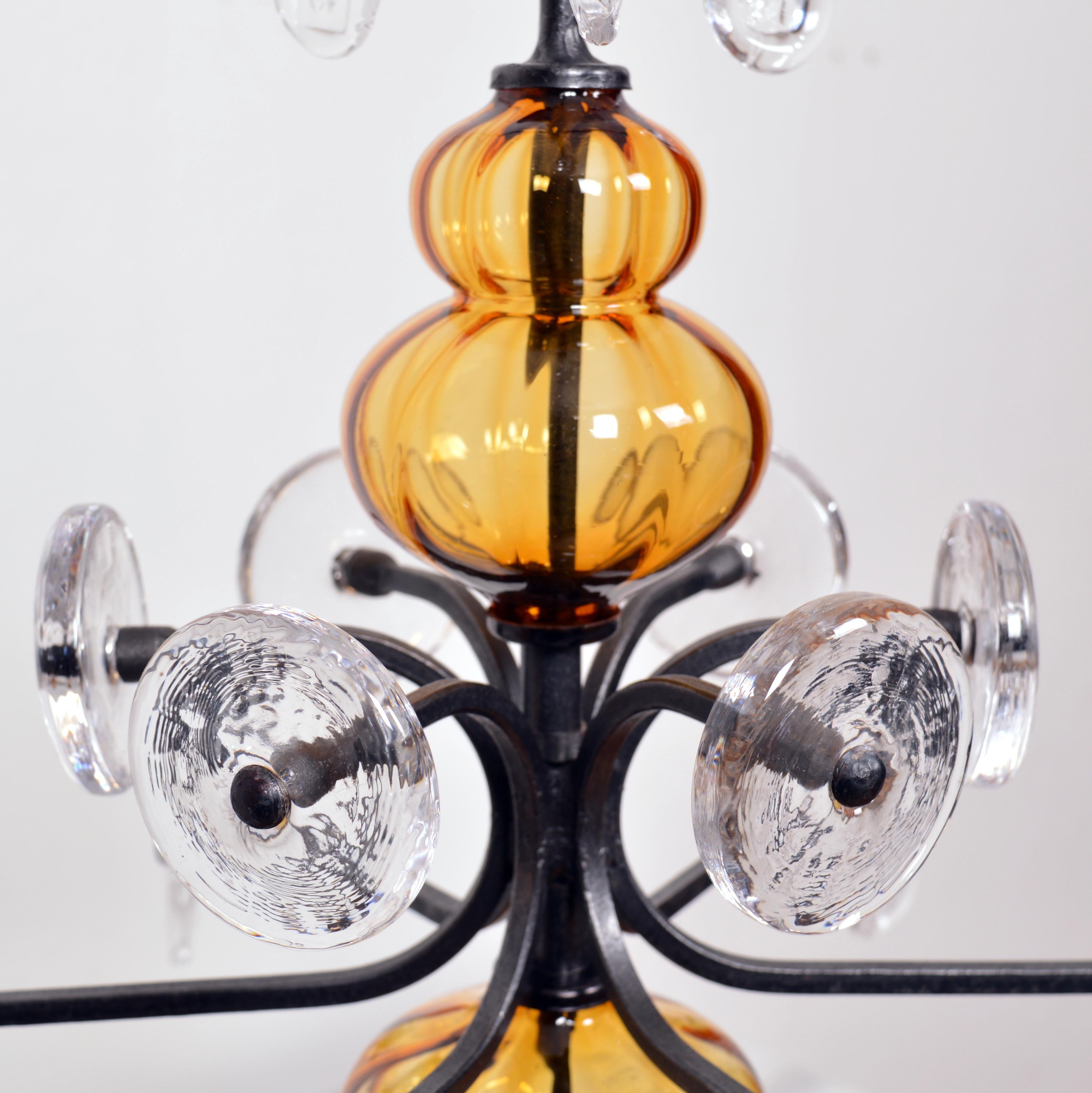 This beautiful amber and clear art glass on wrought iron candelabra chandelier was designed by Erik Höglund for Boda Smide. Erik Höglund (1932–1998) was one of the brightest stars of 20th-century Swedish glass design. This six arm chandelier is in a