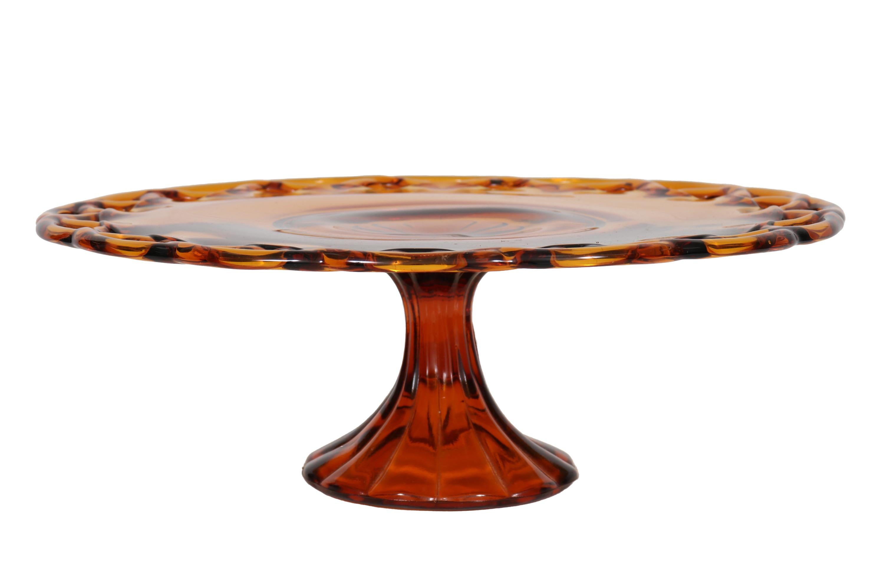 A round amber glass cake stand with a pierced braided edge. The pedestal base is reeded giving a floral center to the cake plate.