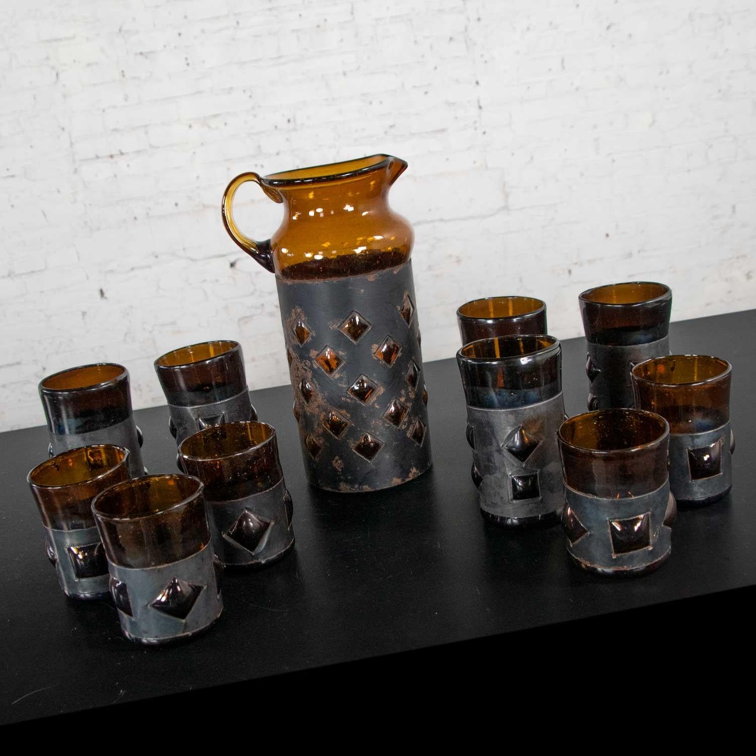 Incredible set of 11 pieces of imprisoned glass brutalist modern Mexican glass cocktail set including 10 tumblers in two sizes and a cocktail pitcher all in amber recycled bottle glass caged by blackened metal bands. Designed and made by Filipe