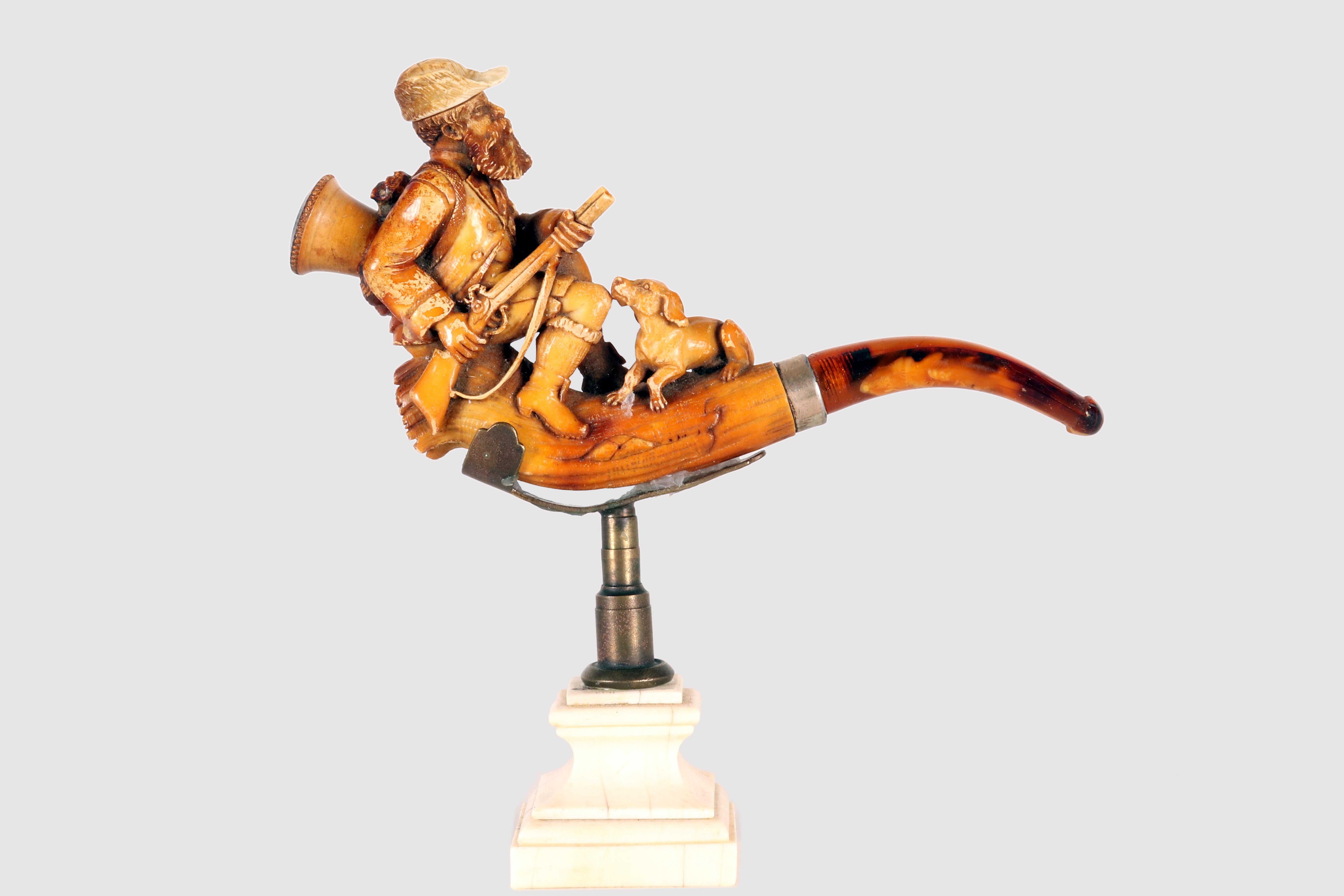 Une pipe à tabac de dégustation, en véritable écume de mer sculptée, avec un embout en ambre véritable. Elle représente un chasseur armé d'un fusil, assis avec son chien. Coffret d'origine en bois, recouvert de cuir.  Vienne, Autriche, fin du XIXe
