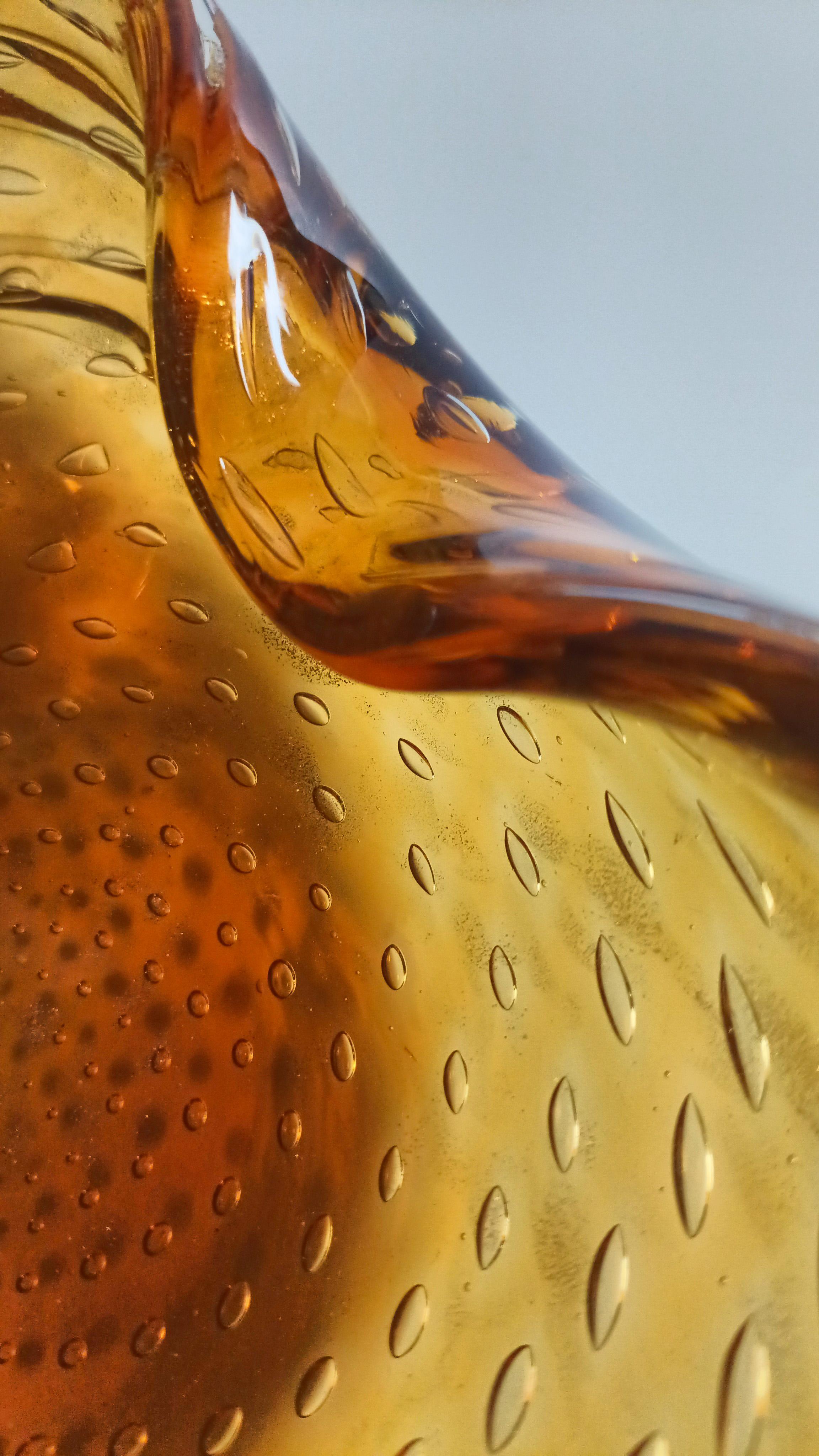 Eine Vintage-Schale aus Murano-Glas in leuchtendem Bernstein, in den 1960er Jahren in Italien mundgeblasen. Die Form ist sanft organisch - eine abgerundete, asymmetrische Muschelform - mit zwei handgezogenen Einbuchtungen auf der Rückseite und einer