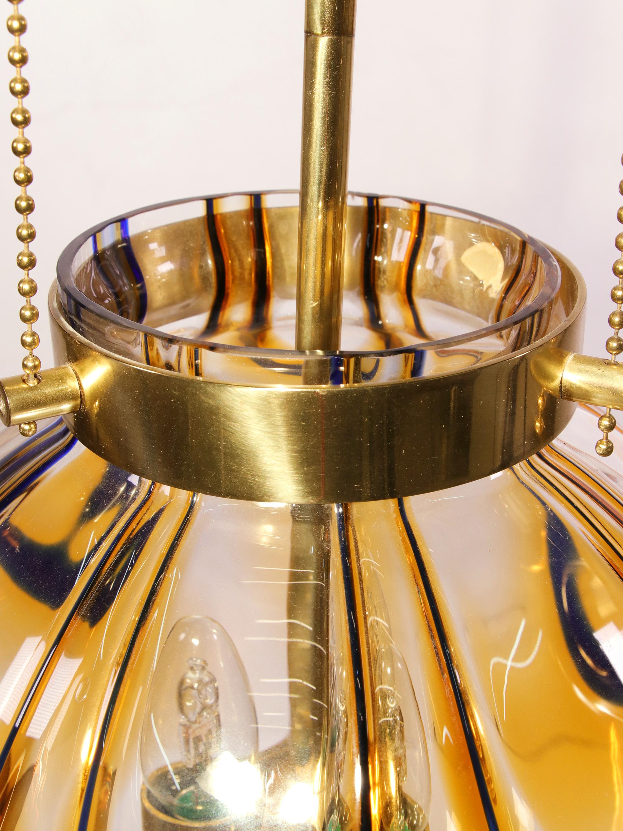 Elégante lampe à suspension avec un globe en verre de Murano ambré et une armature en laiton fixée à trois chaînes. Le lustre éclaire magnifiquement et offre beaucoup de lumière. Gemme de l'époque. Fabriqué par Kaiser Lighting, Allemagne, dans les