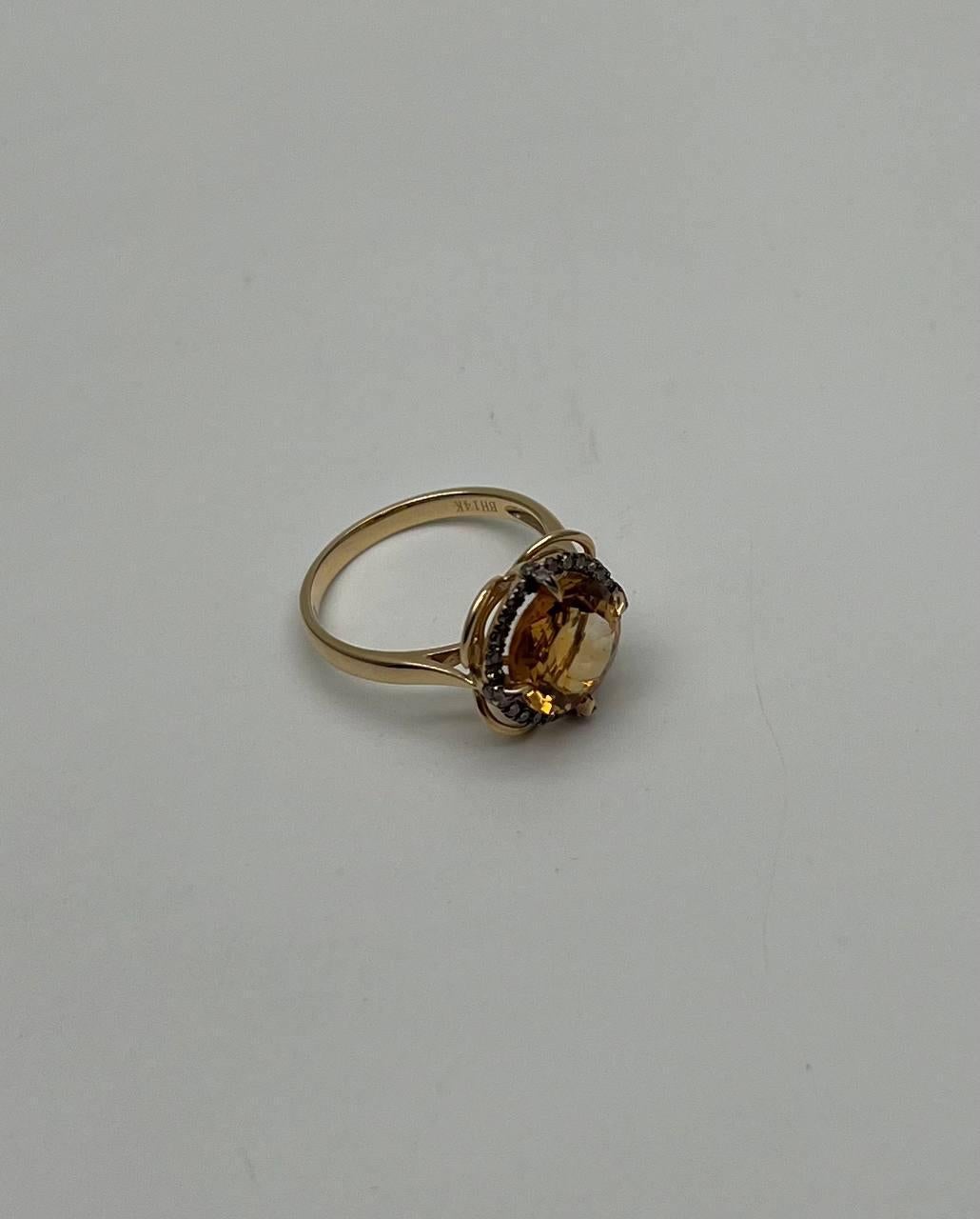 This exquisite ring features a vibrant round orange citrine gemstone at its center, surrounded by a halo of sparkling diamonds. The setting is crafted in a warm gold tone, enhancing the brilliance of the stones. The band is sleek and polished,
