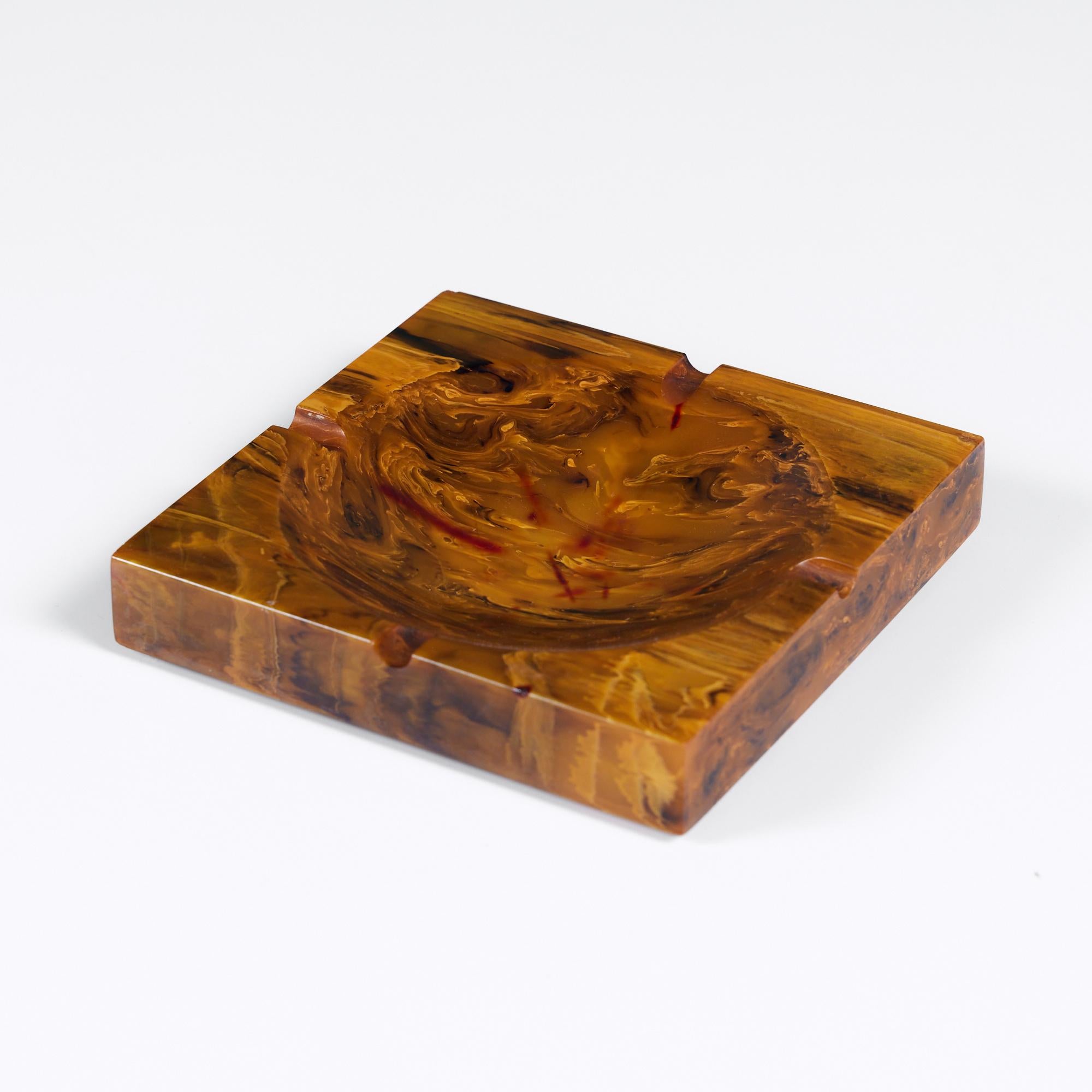 Square ashtray with a low profile and wide bowl in polished resin. The ashtray features an all over tigers eye like pattern. This piece can be used for its original purpose or as a catchall, vide-poche or decorative dish. 

Dimensions
5.75” diameter