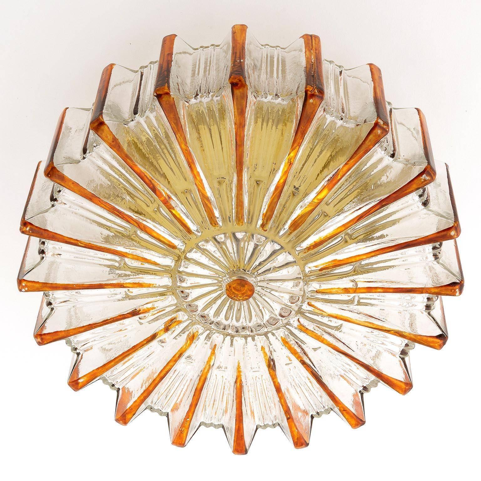 A vintage glass flush mount sunburst sconce, manufactured in Midcentury, circa 1970 (end of 1960s and beginning of 1970s). A glass shade with amber tone rays and gold toned circular back plate.