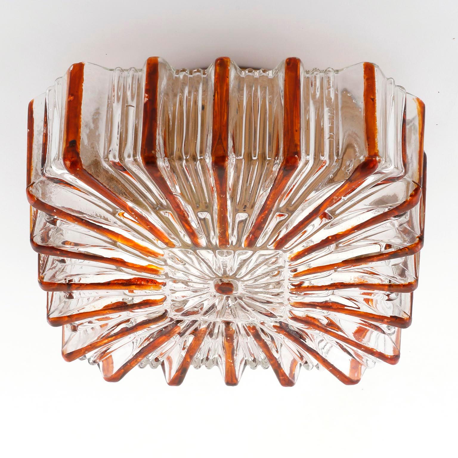A German vintage flush mount or wall light fixture in the style of Glashütte Limburg, manufactured in Midcentury, circa 1970 (late 1960s or early 1970s).
A square, textured, clear glass with an embossed sunburst pattern in an amber color and a gold