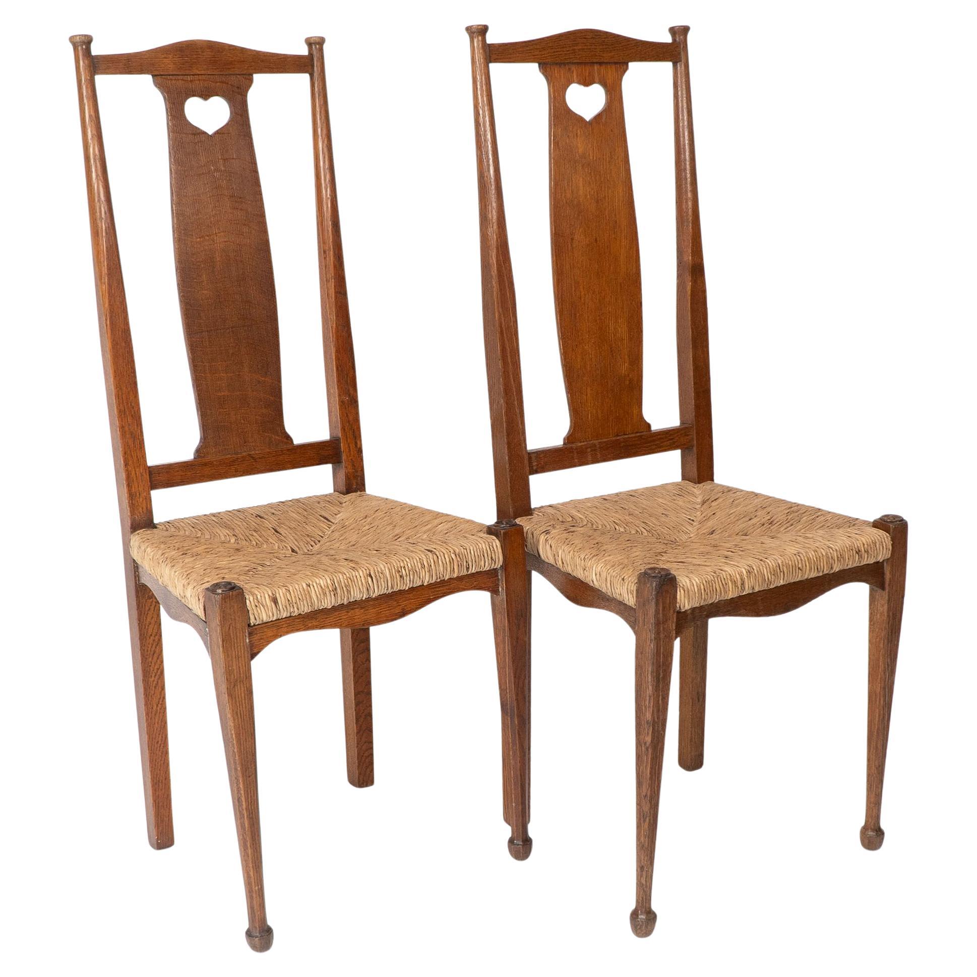 A pair of Arts and Crafts rush seated chairs designed by Ambrose Heals. These chairs are part of one of the first bedroom suits he designed for Heals and Son. These chairs have Voysey's influence of Hearts and simplicity.