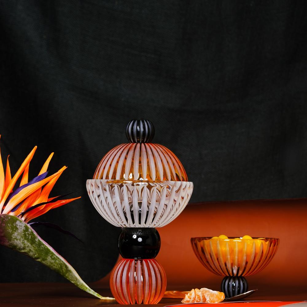 The Ambrosiá footed crystal bowl is a handcrafted, multifunctional centerpiece that blends style and functionality. Its innovative design and look, made of amber, black and clear crystal, effortlessly transitions into two bowls or transforms into a