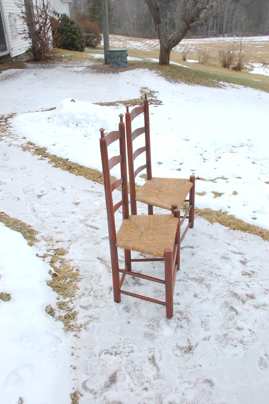 American 18th century pair of ladderback side chairs in ash with original brick red painted surface and delicately turned finials. The finials are integral to the back turnings (not applied). The rush seats are in good condition. These sturdy but