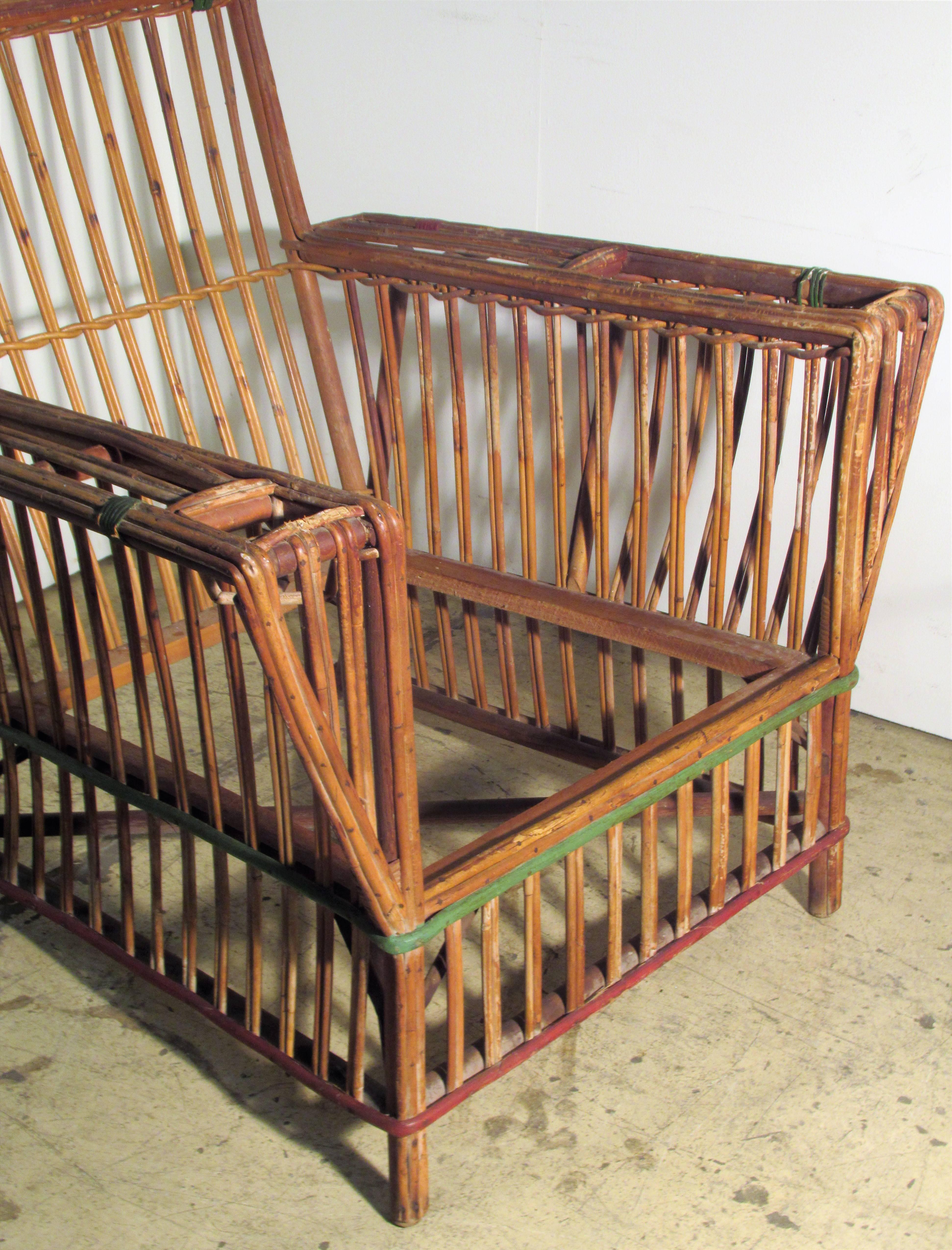 Classic 1930s American Art Deco stick wicker lounge chair with a magazine rack and cup holder at arms. Nicely aged original natural finish retaining period red and green cane wrappings.