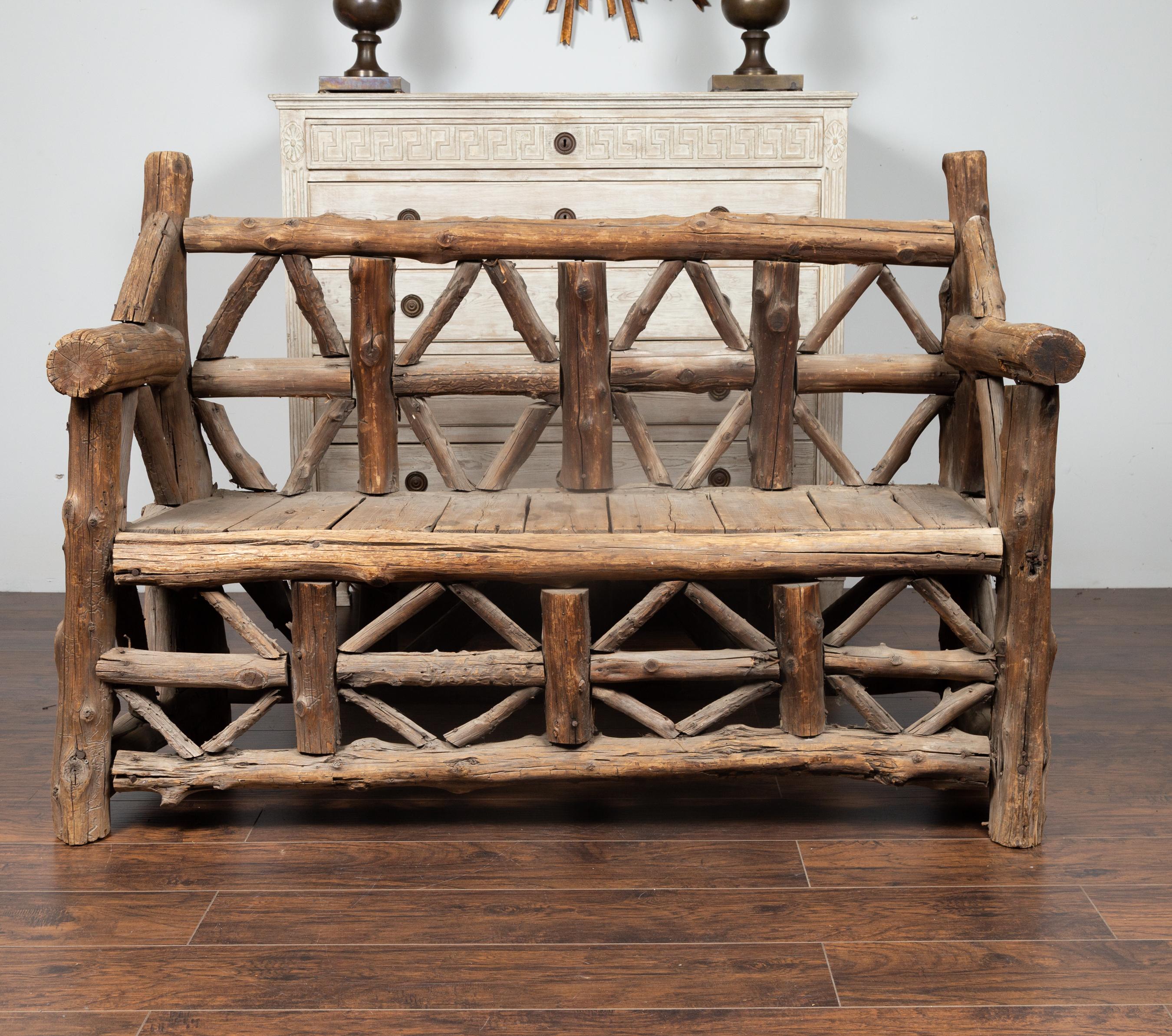 A large American rustic bench from the early 20th century, made of logs. Born during the second quarter of the 20th century, this wooden bench charms us with its rustic appearance and weathered patina. Made of logs arranged in geometric patterns and