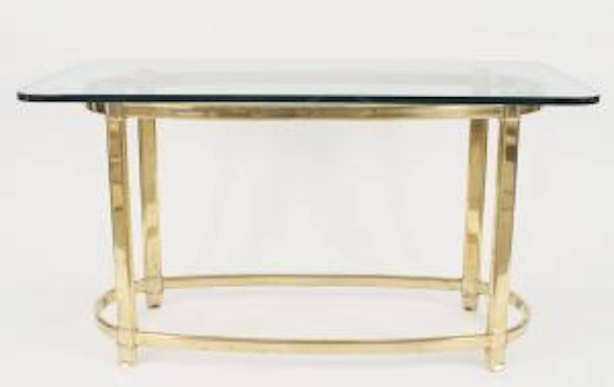 Table de centre de style américain des années 1940 avec une base ovale en laiton avec un brancard ovale supportant un plateau en verre rectangulaire.
   