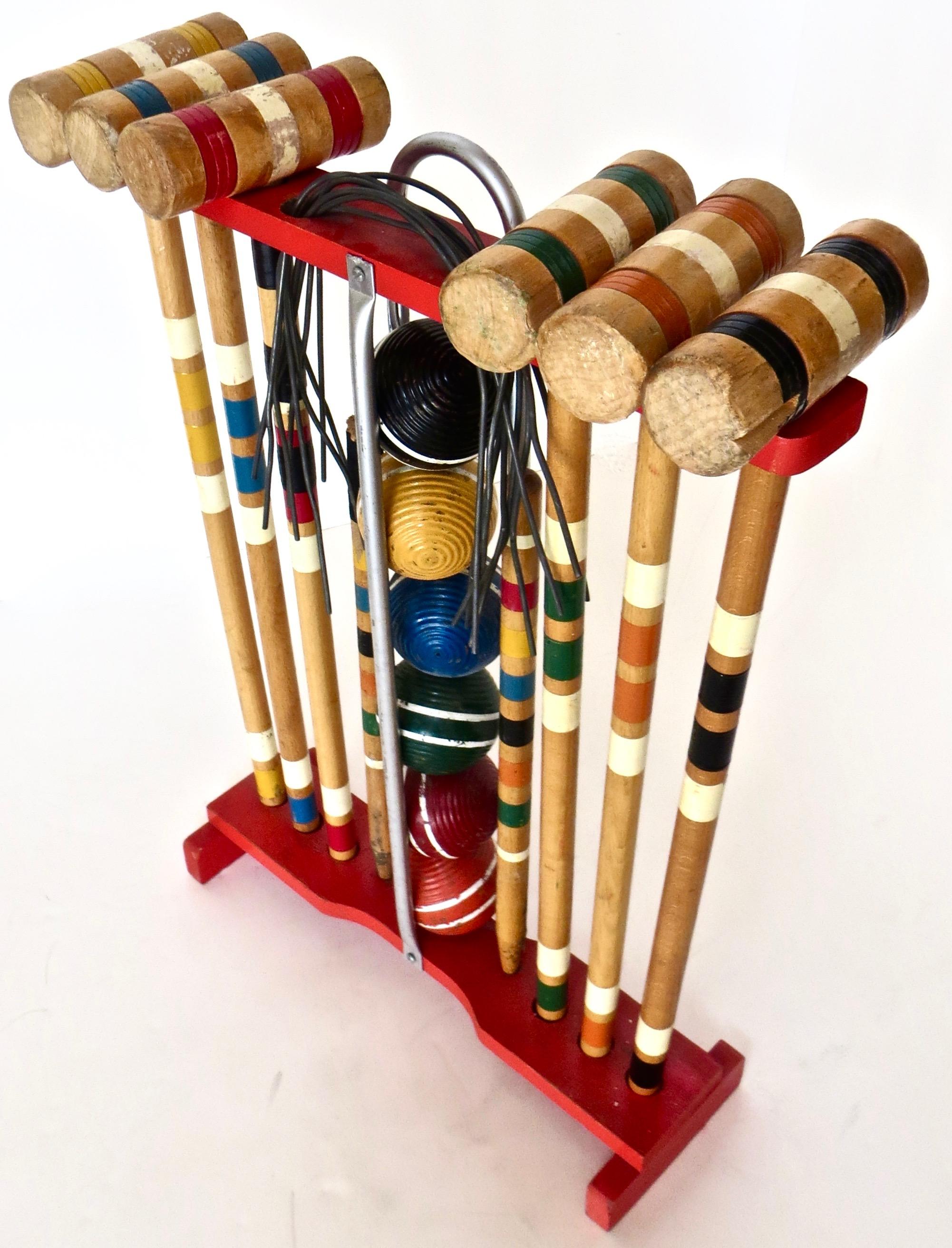 1950s outdoor wooden croquet set on a red stand; for six players with six different color balls; black, yellow, blue, green, red, and orange, all with a double white stripe around the circumference; with matching croquet mallets; along with two end