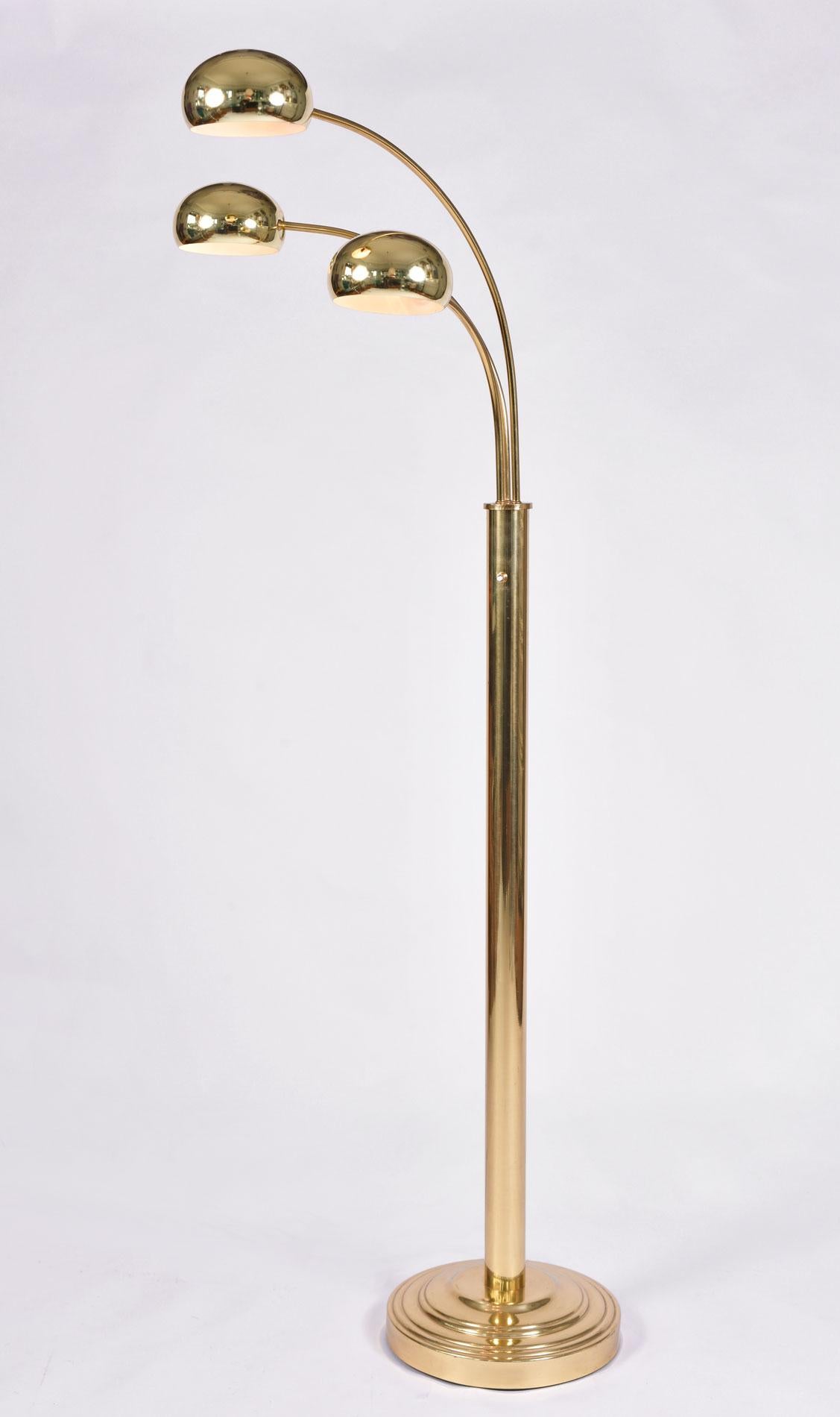 Tall brass arched floor lamp with three arms. Brass tiered base with brass stem from which depart three different lengths adjustable arches, each with a semi circular brass shade.