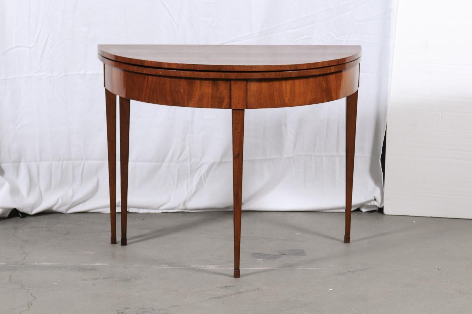 American, first quarter 19th century; probably Mid-Atlantic. A Hepplewhite Demi-Lune mahogany card table with flip top, swing leg, raised on square tapered legs with a slight foot. Approx. H 30