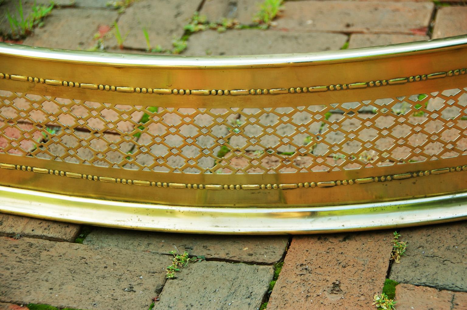 American late 19th century serpentine brass pierced fender with two brass balls on each return; 59 1/2 inches long. There are small bruises to the top rail of the fender.